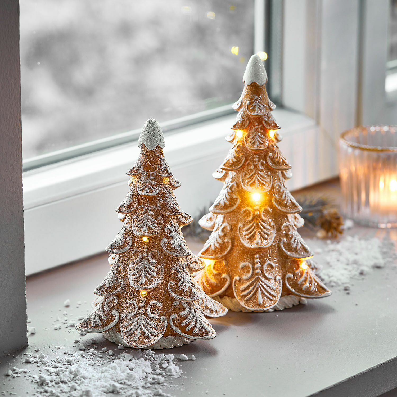 Zwei dekorative Keramik-Weihnachtsbäume mit LED-Beleuchtung und weißem Schnee-Effekt auf Fensterbank