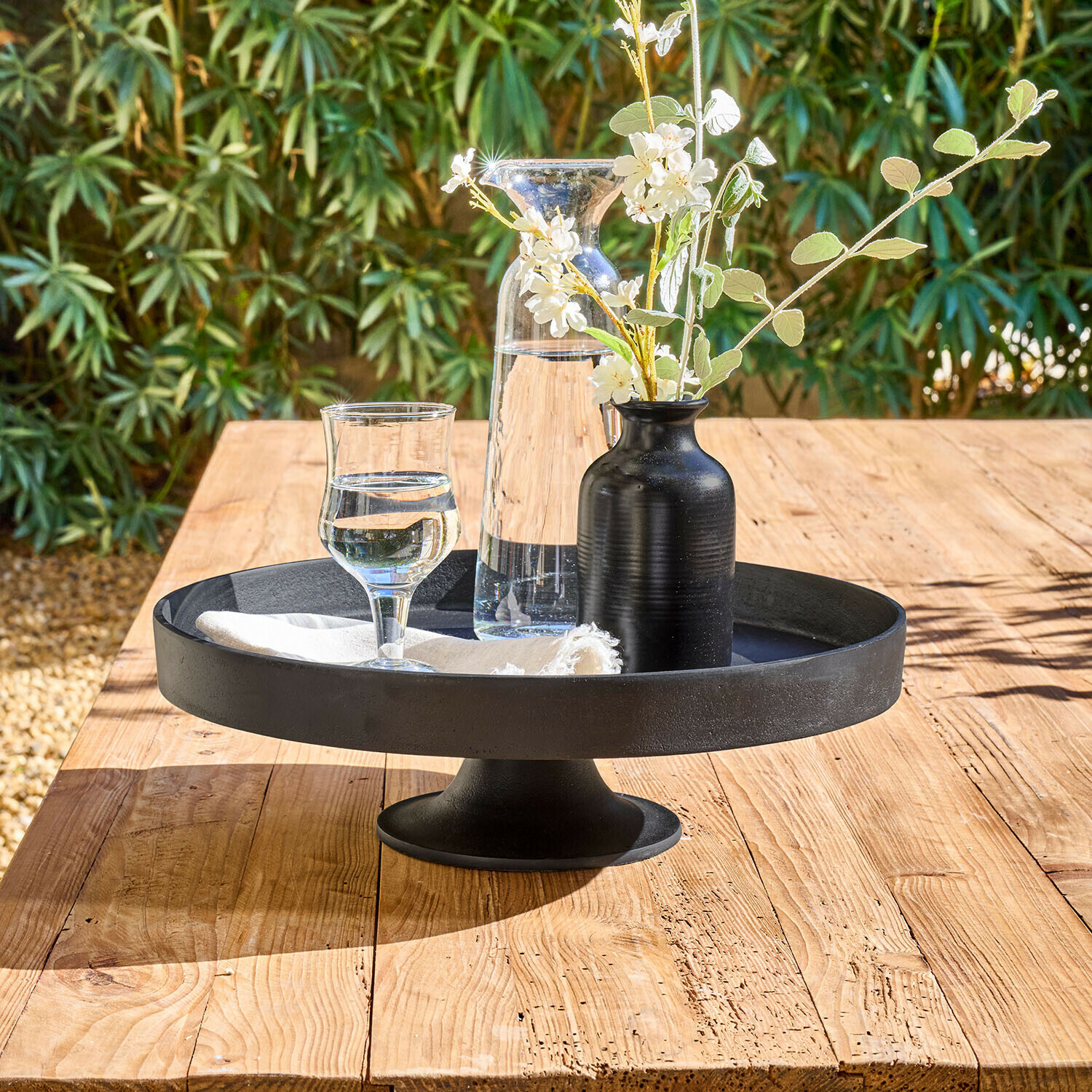 Schwarze Metall-Etagere mit Karaffe, Glas und schwarzer Blumenvase auf hellem Holztisch