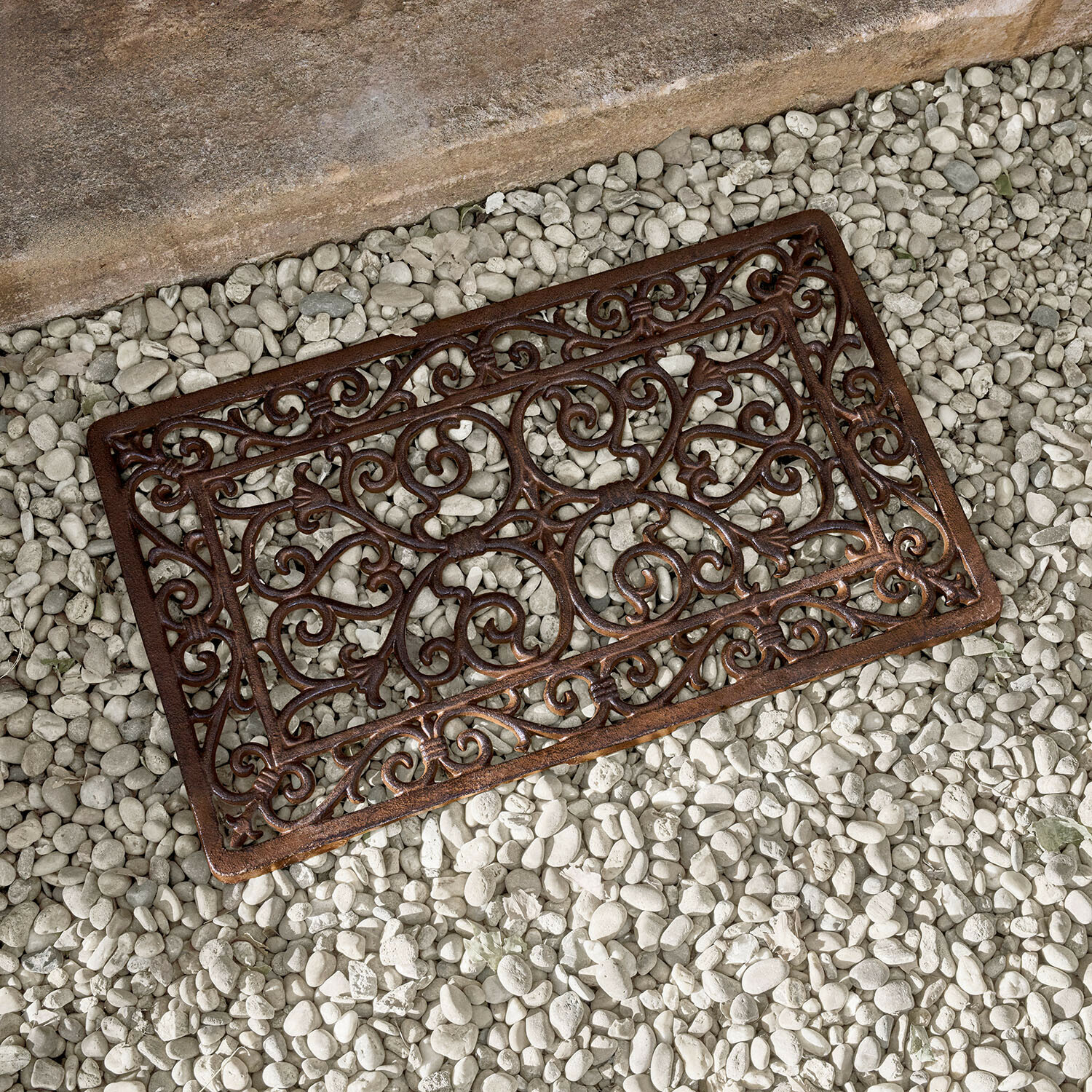 Braune Metallmatte mit dekorativem Muster auf weissen Steinen, gusseiserne Fussmatte