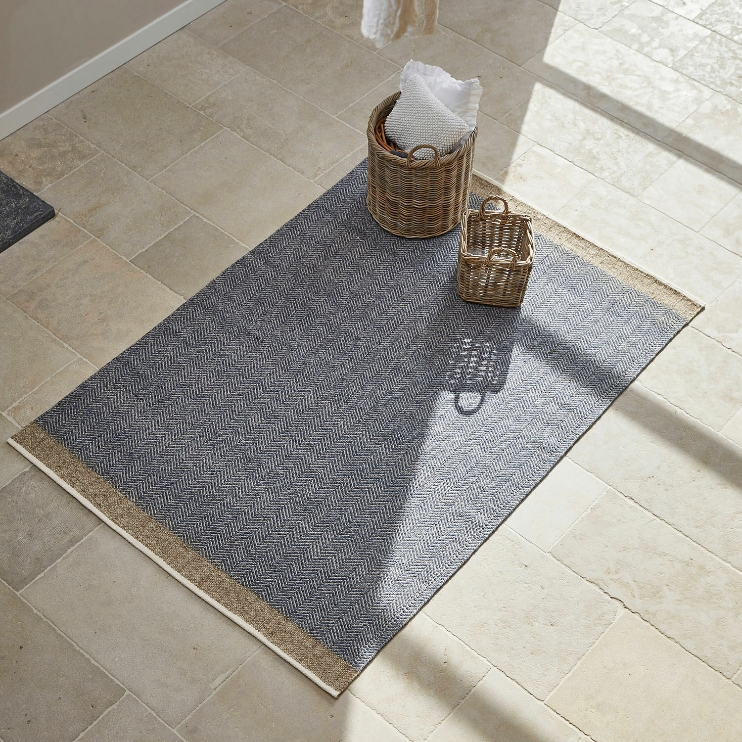 Grau gemusterter Teppich mit Fischgrätmuster und Naturkanten auf hellem Boden mit Körben