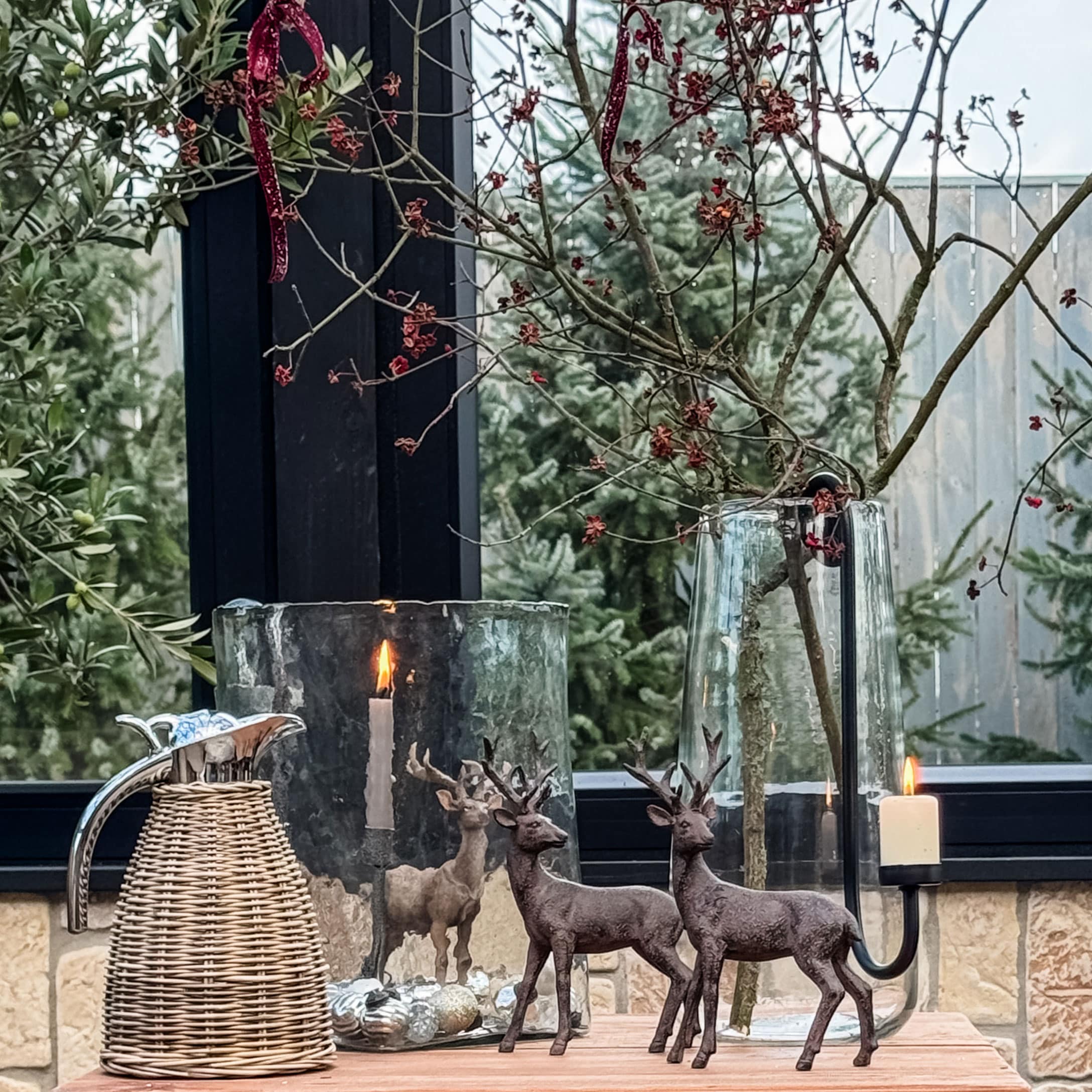 Weihnachtliche Dekoration mit zwei braunen Hirschfiguren, Glaswindlicht und Rattankrug auf Holztisch