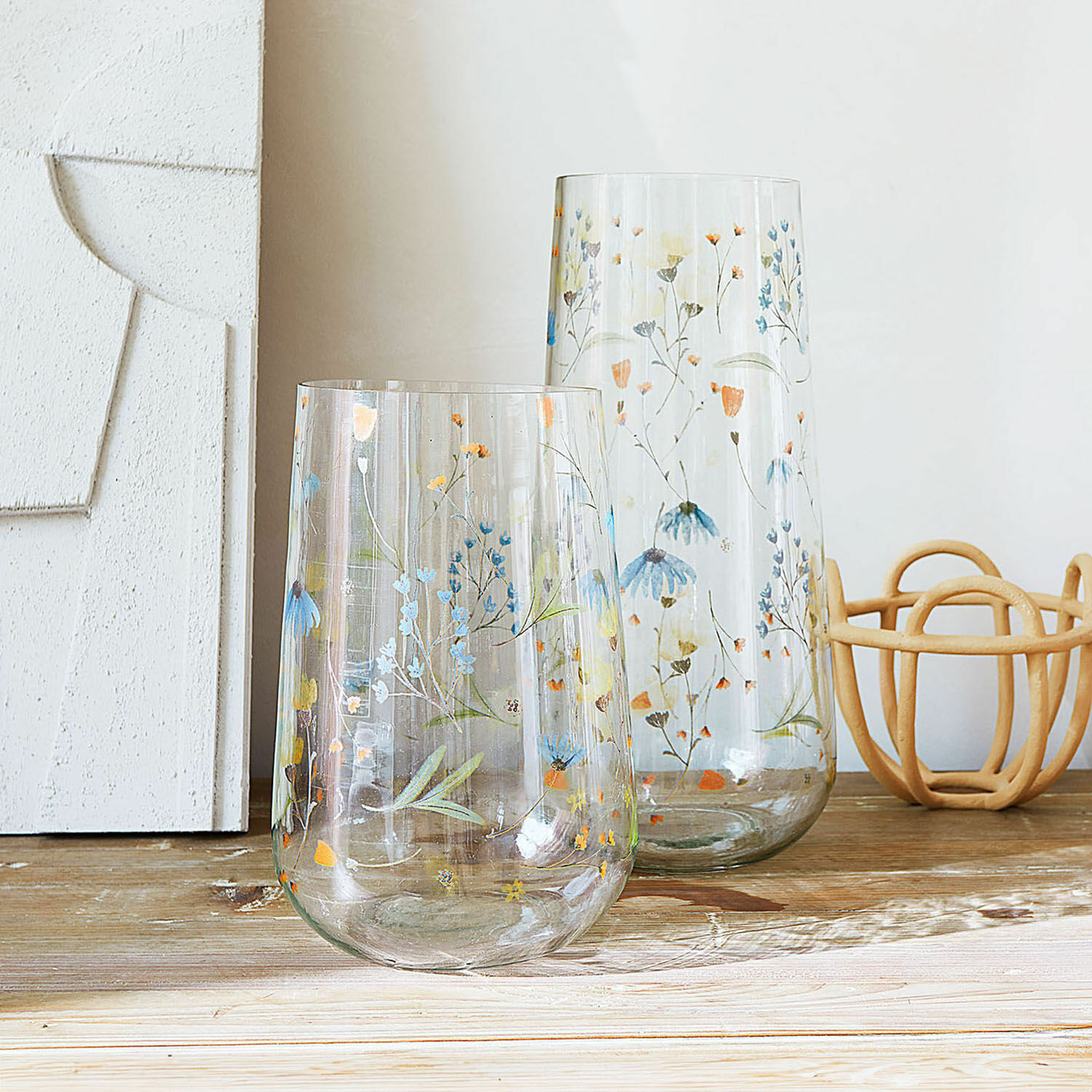 Vase 2er Set Nervila Zwei transparente Glasvasen mit buntem Blumenmuster dekorativ auf einem Holztisch arrangiert.