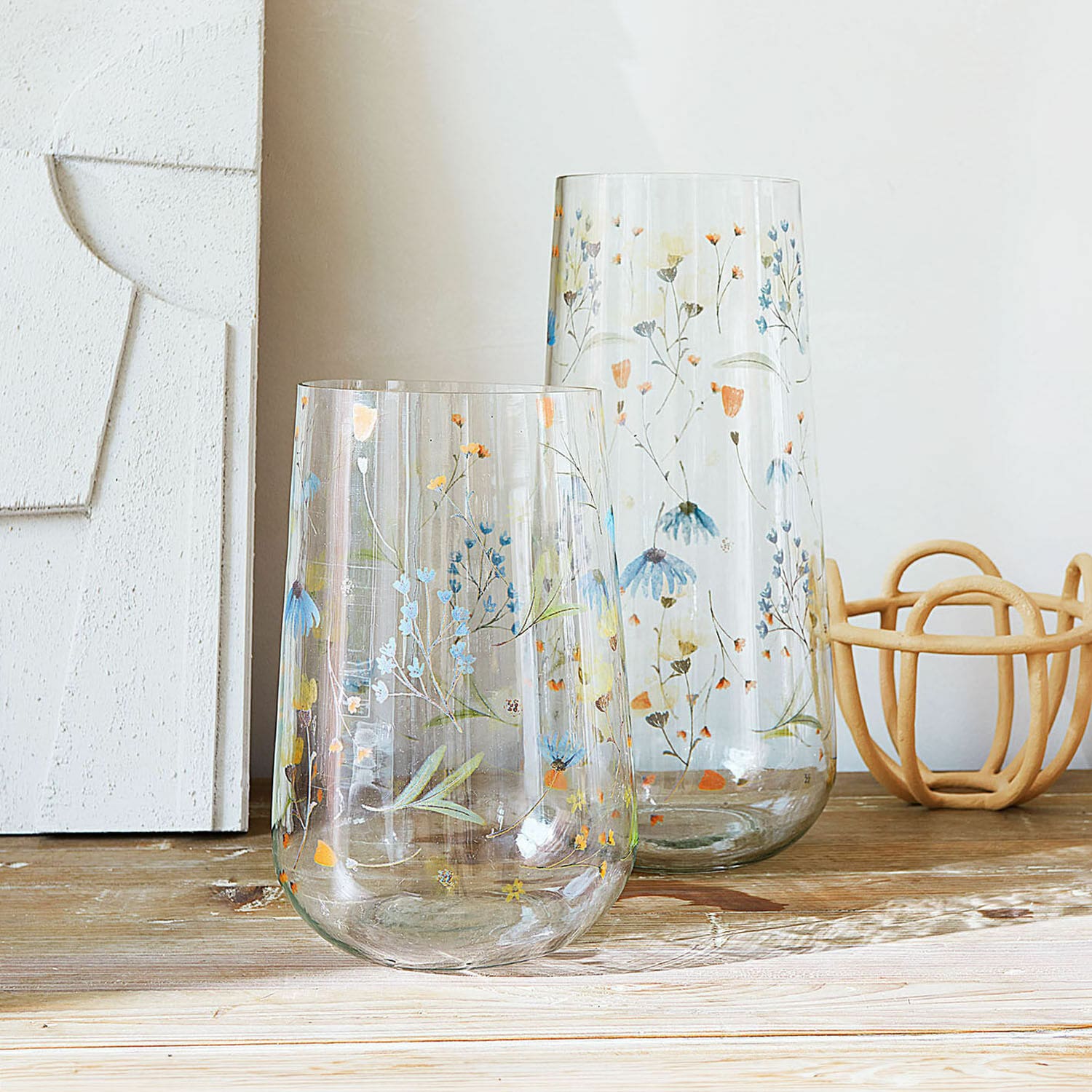 Vase 2er Set Nervila Zwei transparente Glasvasen mit buntem Blumenmuster dekorativ auf einem Holztisch arrangiert.