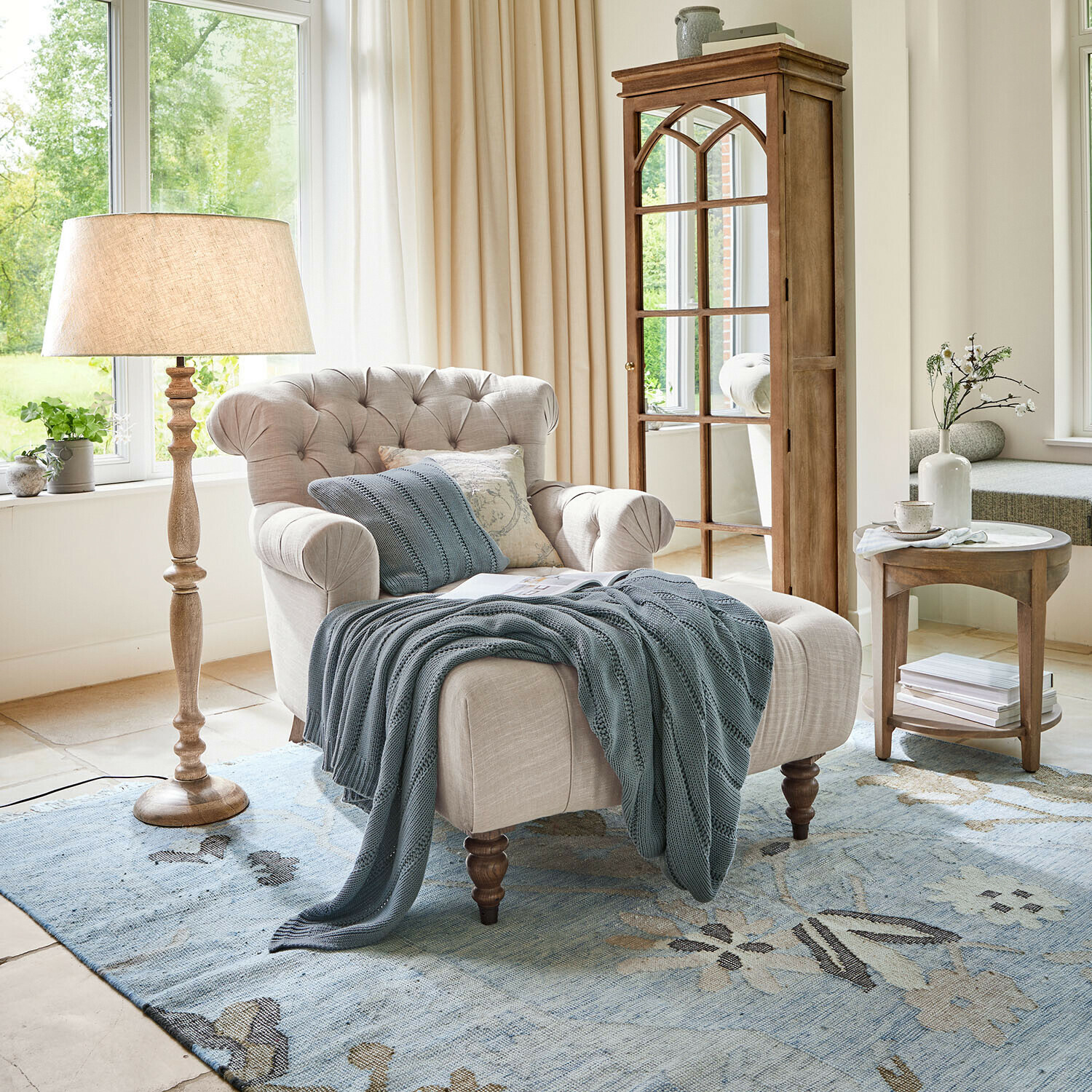 Chaiselongue Springfield Village Beiger Polsterstuhl mit gesteppter Rückenlehne und blauem Strickplaid auf blauem Teppich im hellen Wohnzimmer