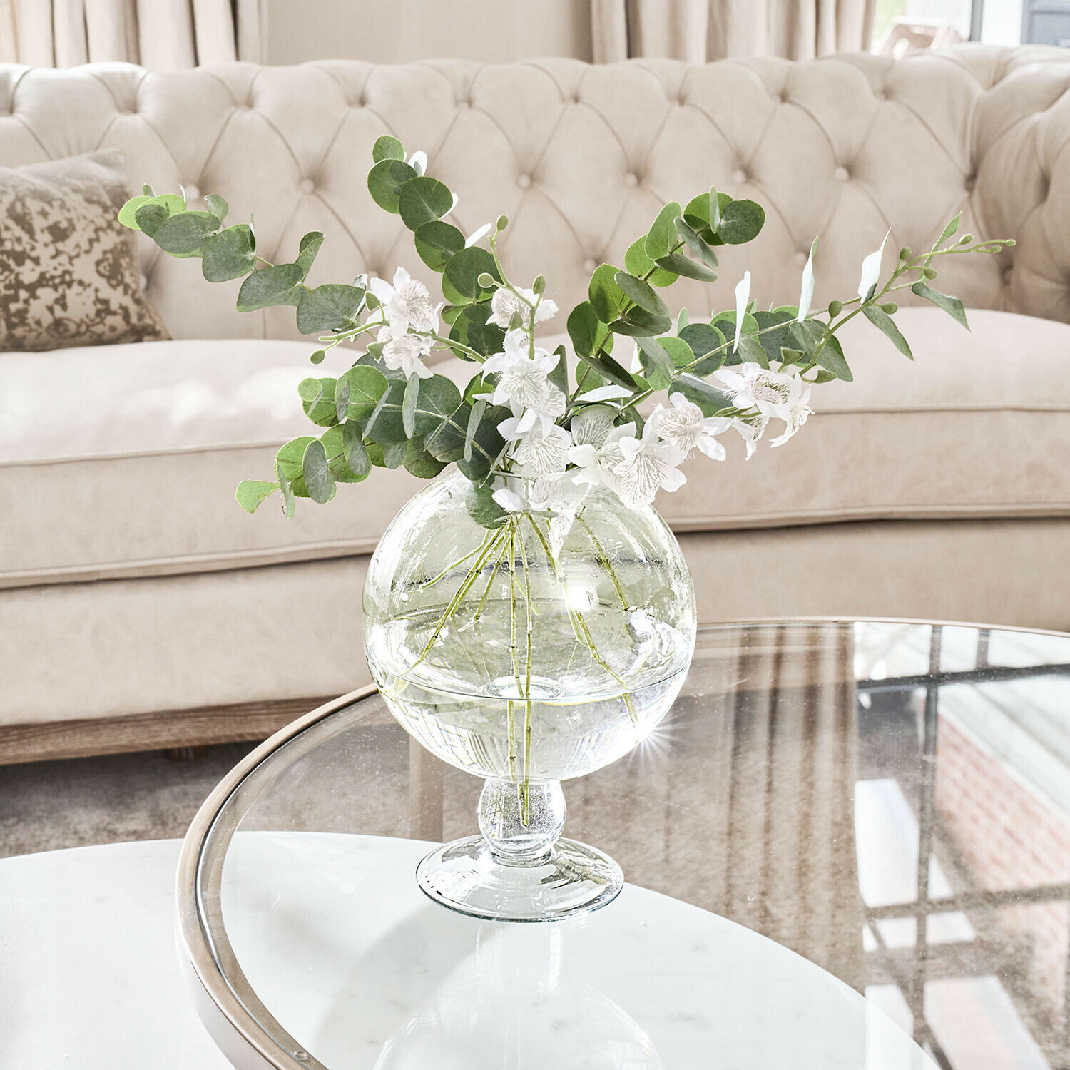 Vase Marsetta Transparente Glasvase mit grünen Blättern und weissen Blumen auf Glastisch im hellen Wohnzimmer