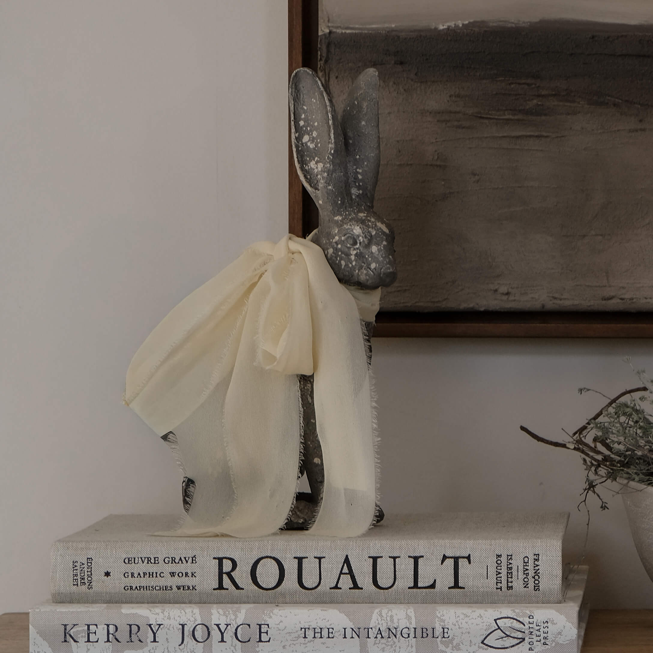 Dekorativer grauer Hase mit cremefarbenem Stoffschal auf einem Stapel Vintage-Bücher
