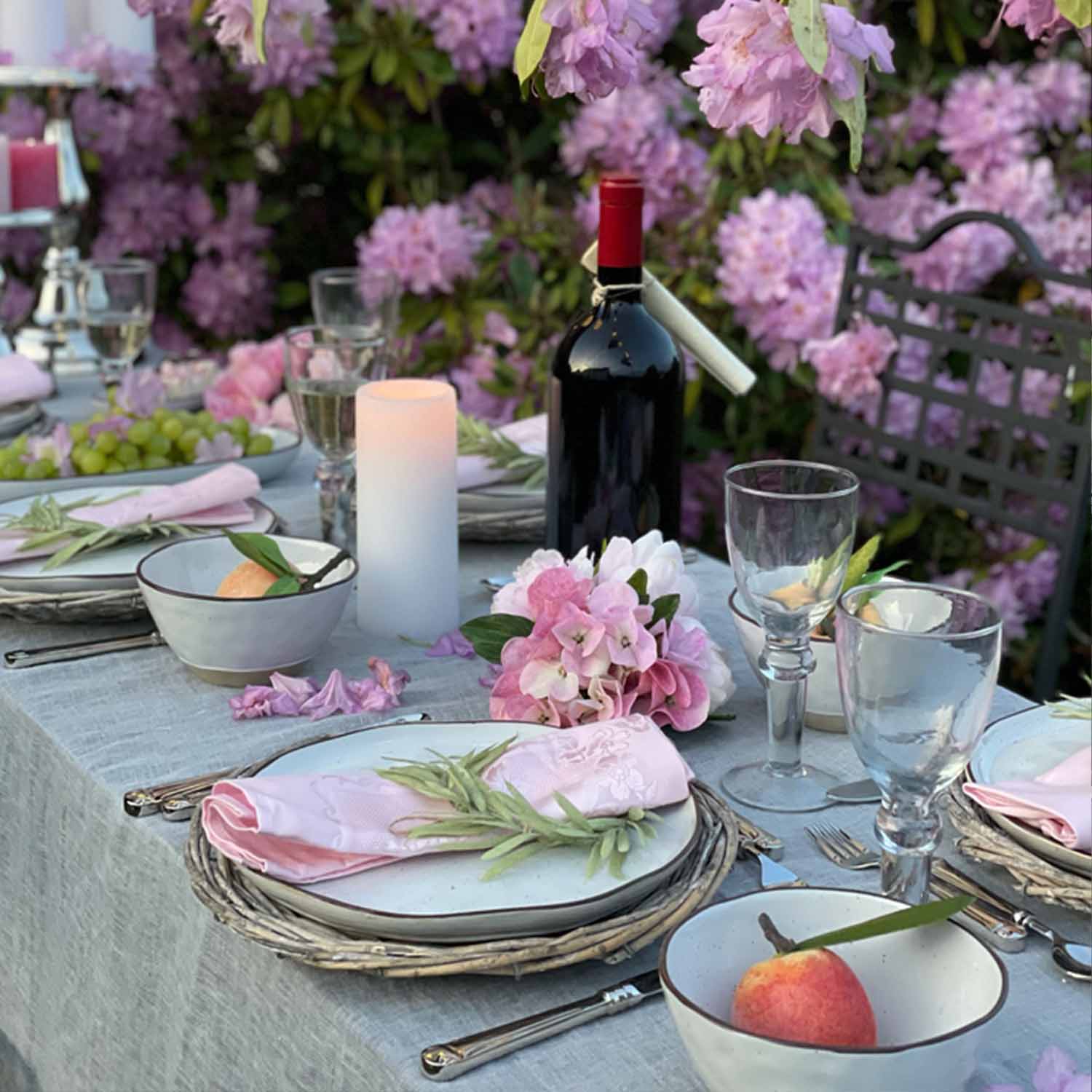 Eleganter gedeckter Tisch mit weissem Geschirr, rosa Servietten und rotem Wein in blühendem Garten