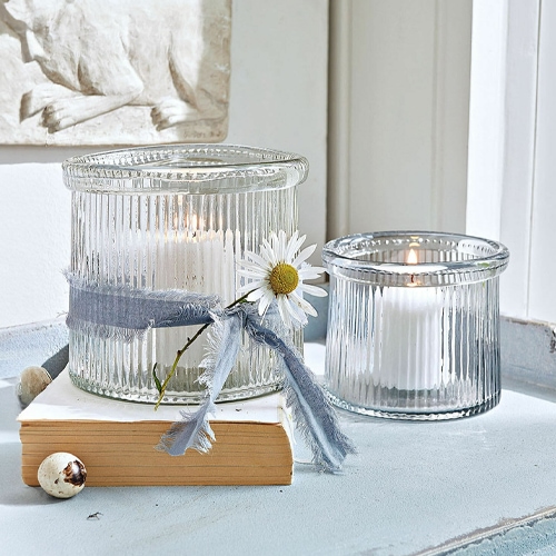 Glaswindlichter aus geriffeltem Glas mit weissen Kerzen und dekorativem Band mit Blume.
