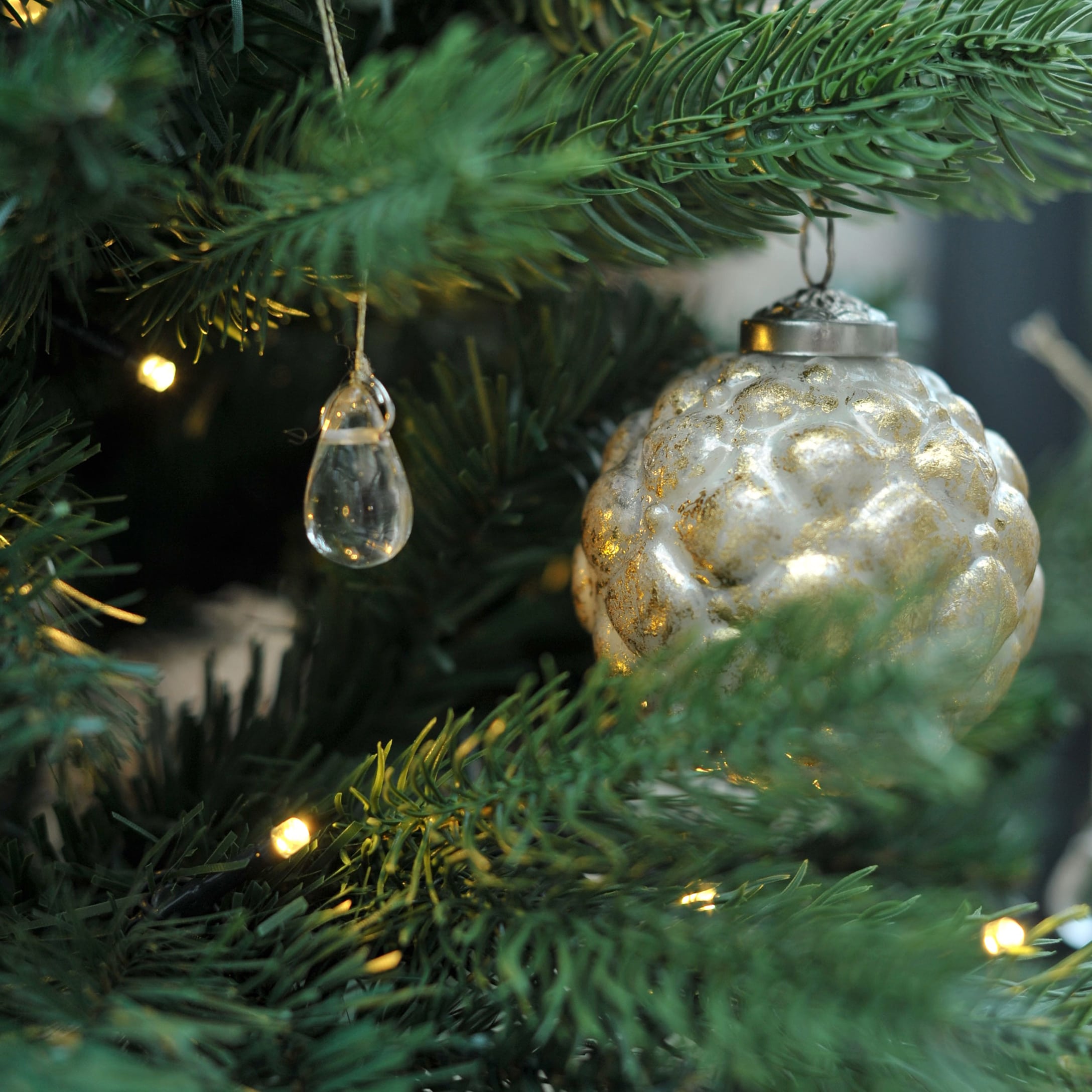Goldene Glas-Weihnachtskugel und transparente Anhänger am grünen Tannenbaum mit Lichterkette