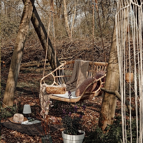 Gartenschaukel aus natürlichem Rattan mit Kissen und Decke vor herbstlichem Waldhintergrund