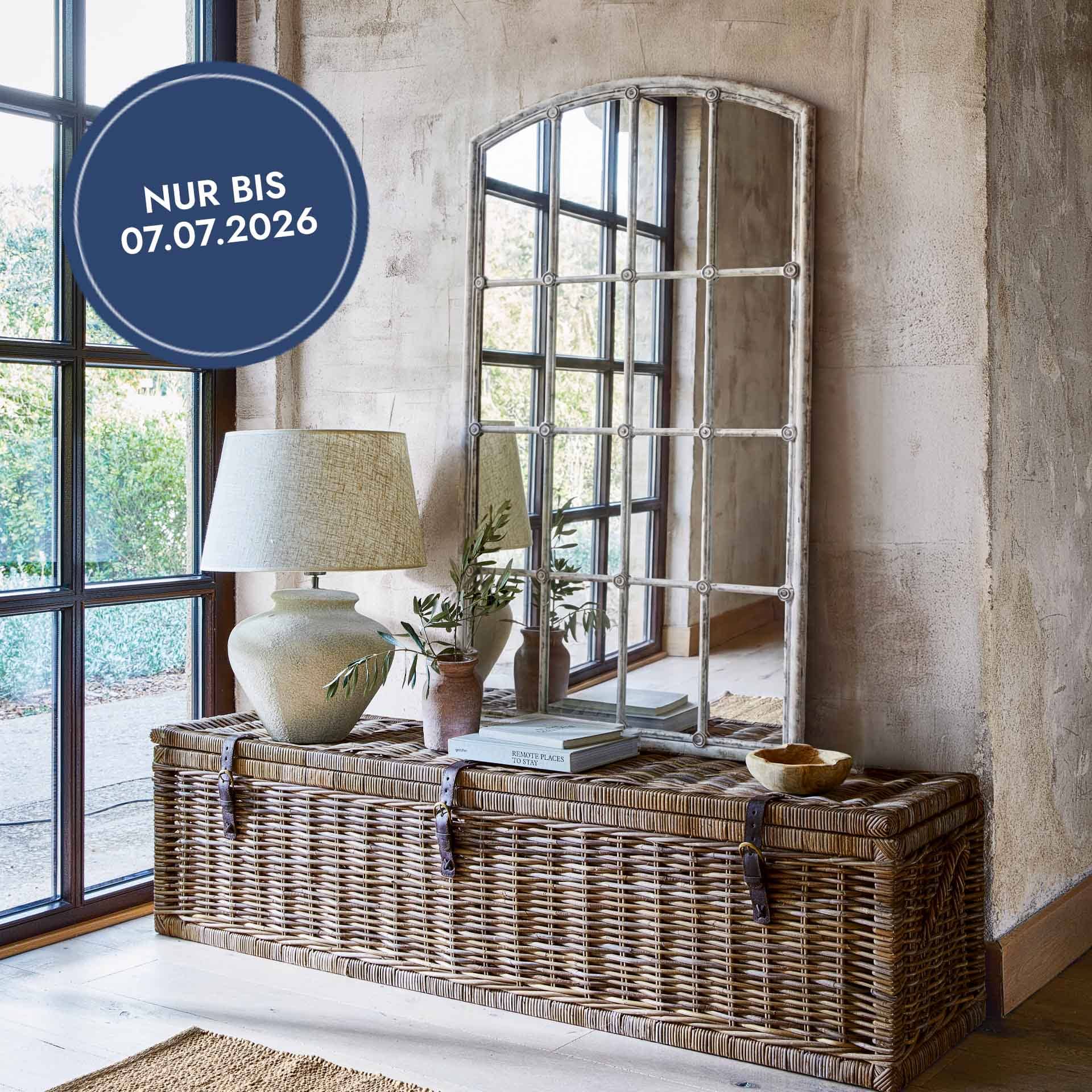 Grosse Rattantruhe in Naturfarbe mit Lampe und Vintage-Spiegel in hellem Wohnzimmer