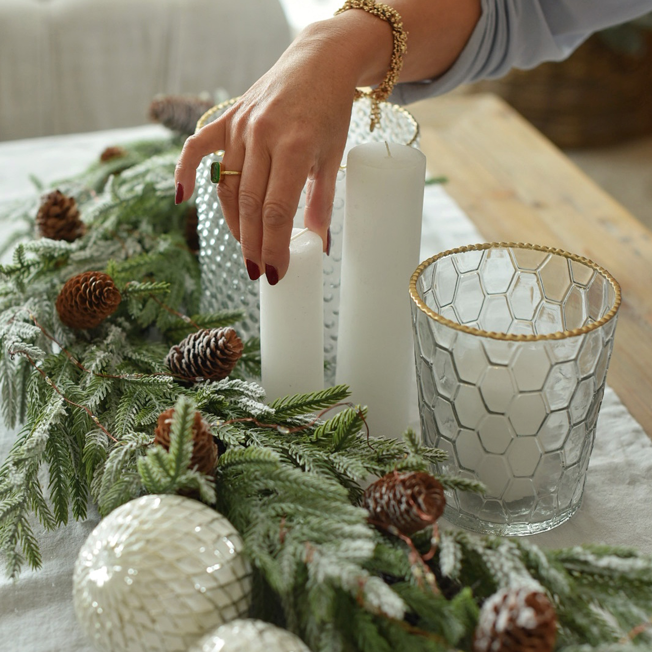 Weihnachtsdekoration mit weissen Kerzen, Glaswindlicht mit goldenem Rand und grünen Zweigen mit Zapfen