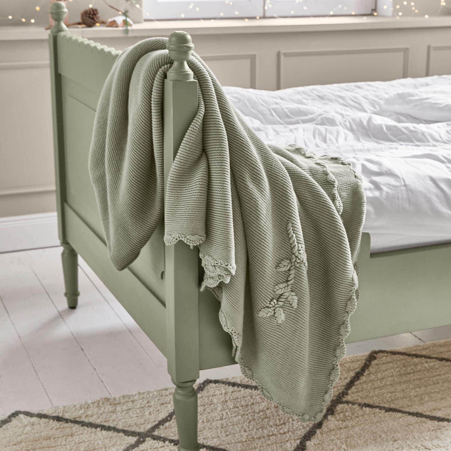 Mintgrüne Baumwolldecke mit dekorativer Stickerei auf grünem Holzbett im Schlafzimmer