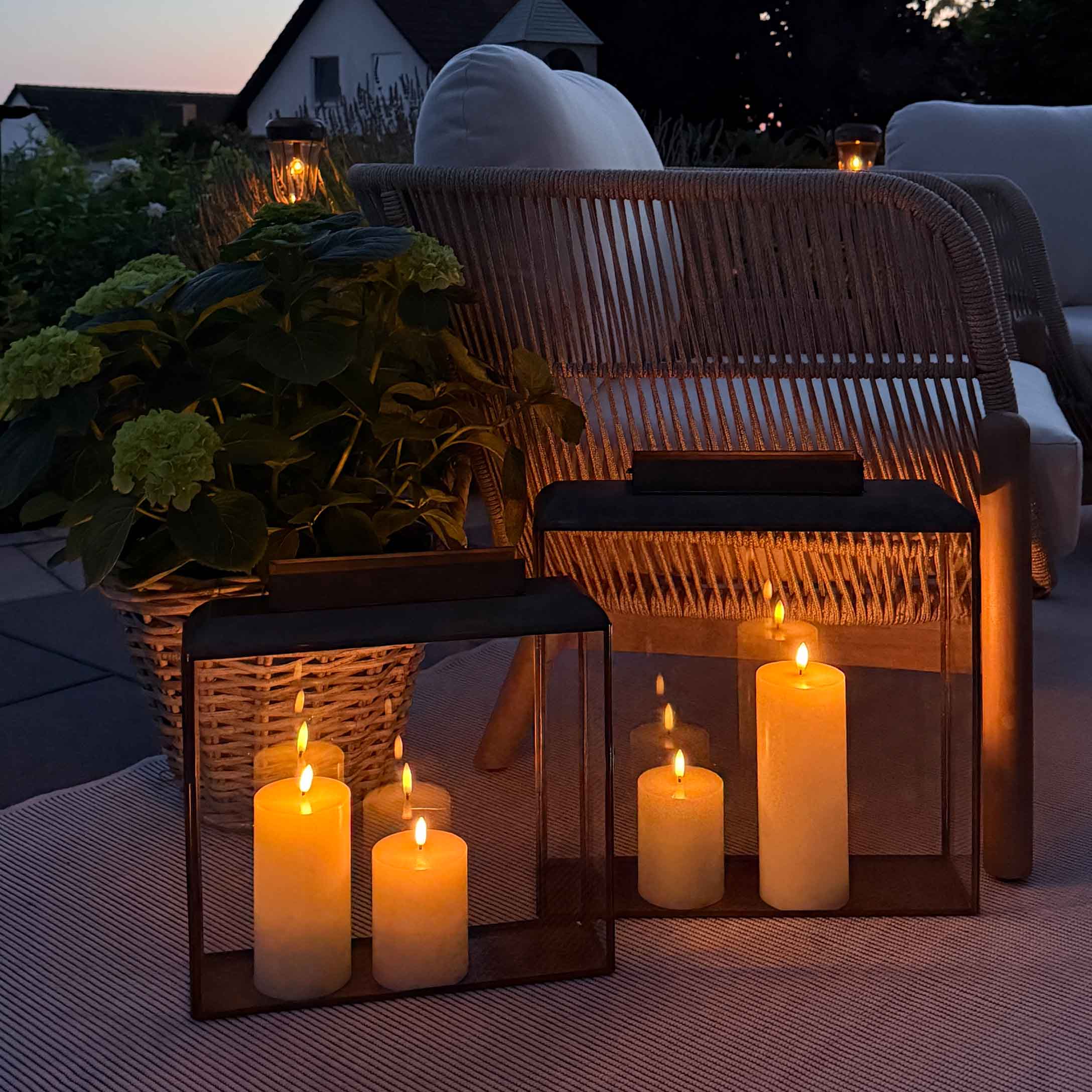 Stimmige Beleuchtung mit Laternen und Kerzen auf Terrasse mit Korbsessel und weissem Kissen