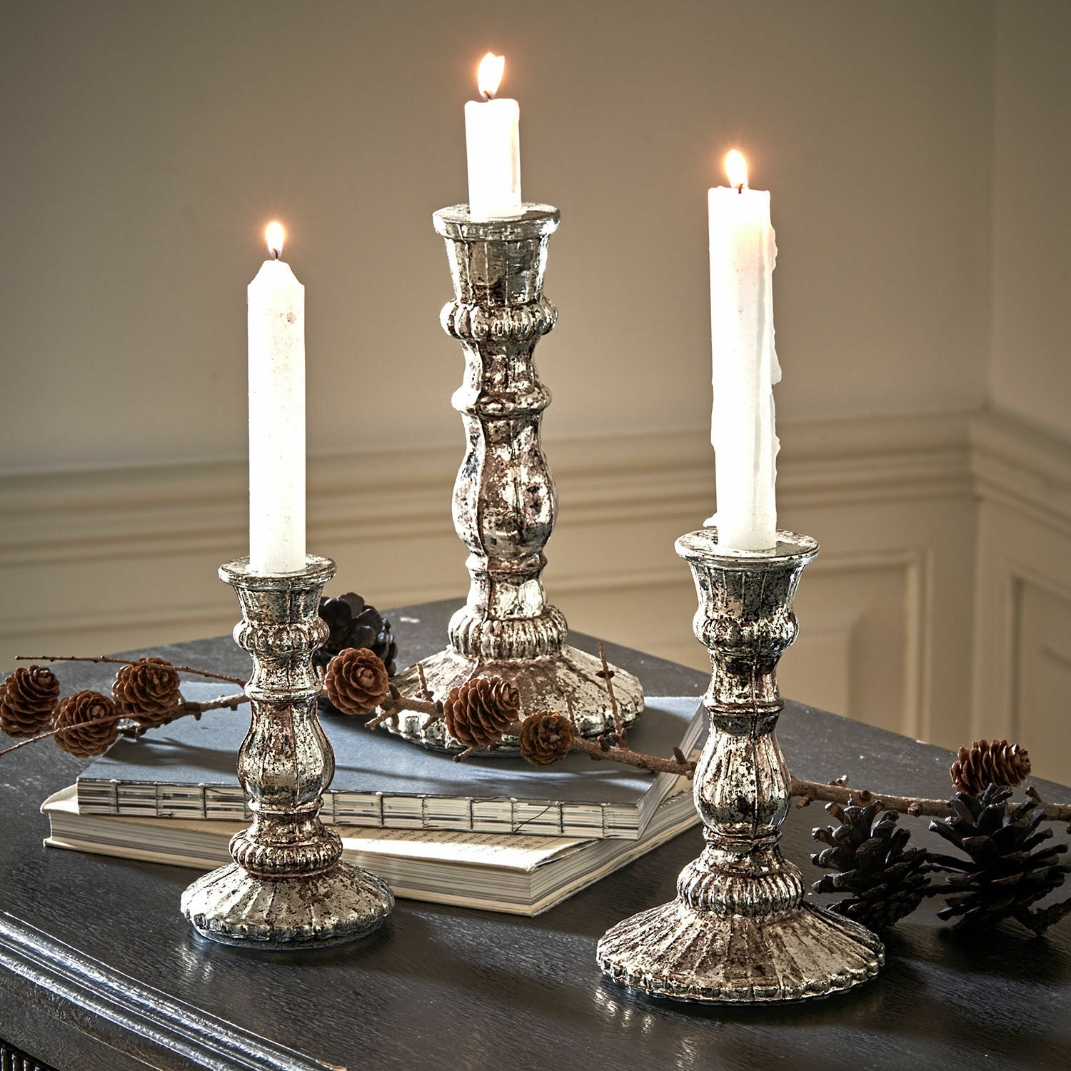 Kerzenständer 3er Set Favalina Drei vintage Metall-Kerzenhalter in Silber mit weissen Kerzen auf dunklem Tisch mit Kiefernzapfen dekoriert