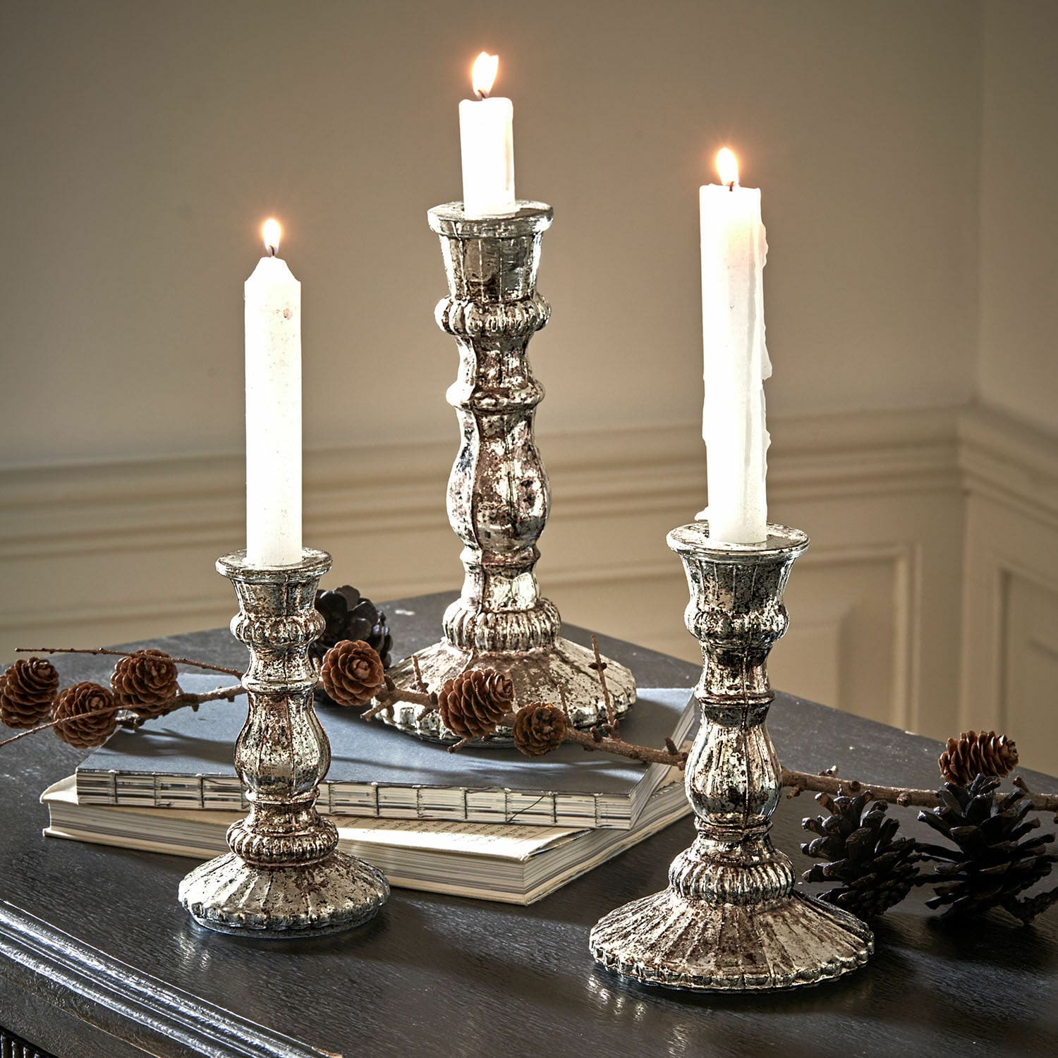Kerzenständer 3er Set Favalina Drei vintage Metall-Kerzenhalter in Silber mit weissen Kerzen auf dunklem Tisch mit Kiefernzapfen dekoriert