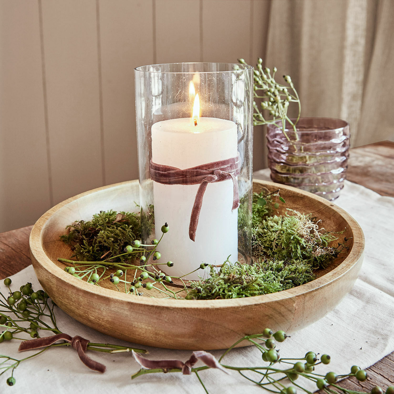 Weisse Kerze im Glaszylinder mit Samtband auf Holztablett, dekoriert mit grünem Moos