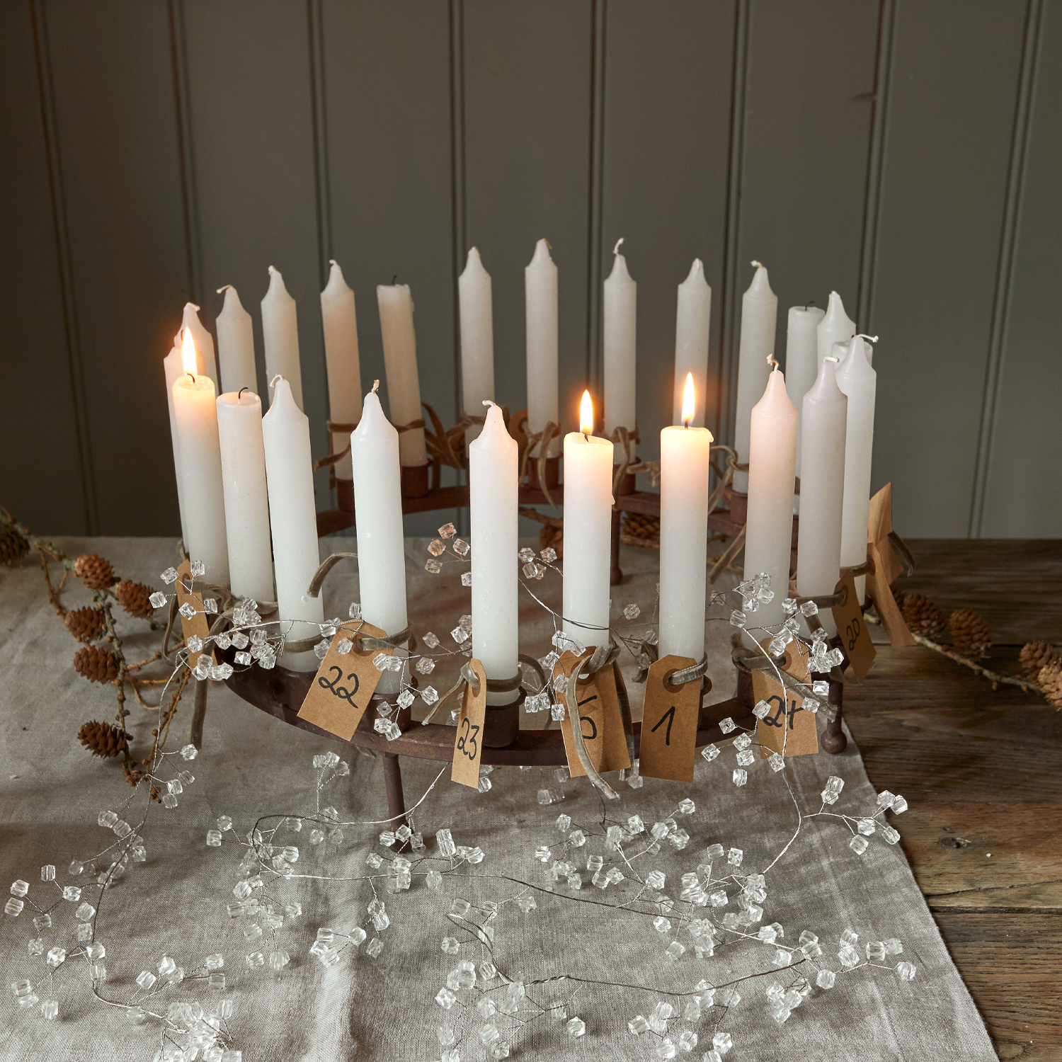 Metall-Adventskranz mit 24 weissen Kerzen und nummerierten Papieranhängern auf Leinentuch