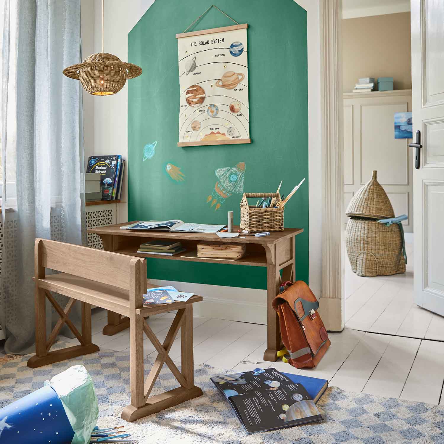 Holzschreibtisch und Bank im Kinderzimmer mit grüner Wand und Sonnensystem-Poster