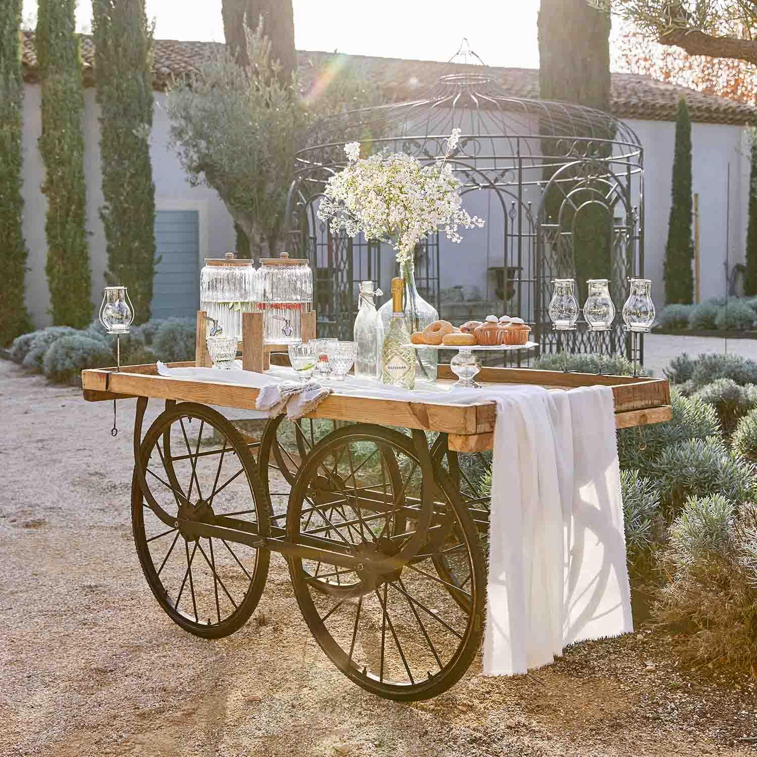 Holzwagen mit Metallrädern, dekoriert mit Glasbehältern und Blumen in einem sonnigen Garten