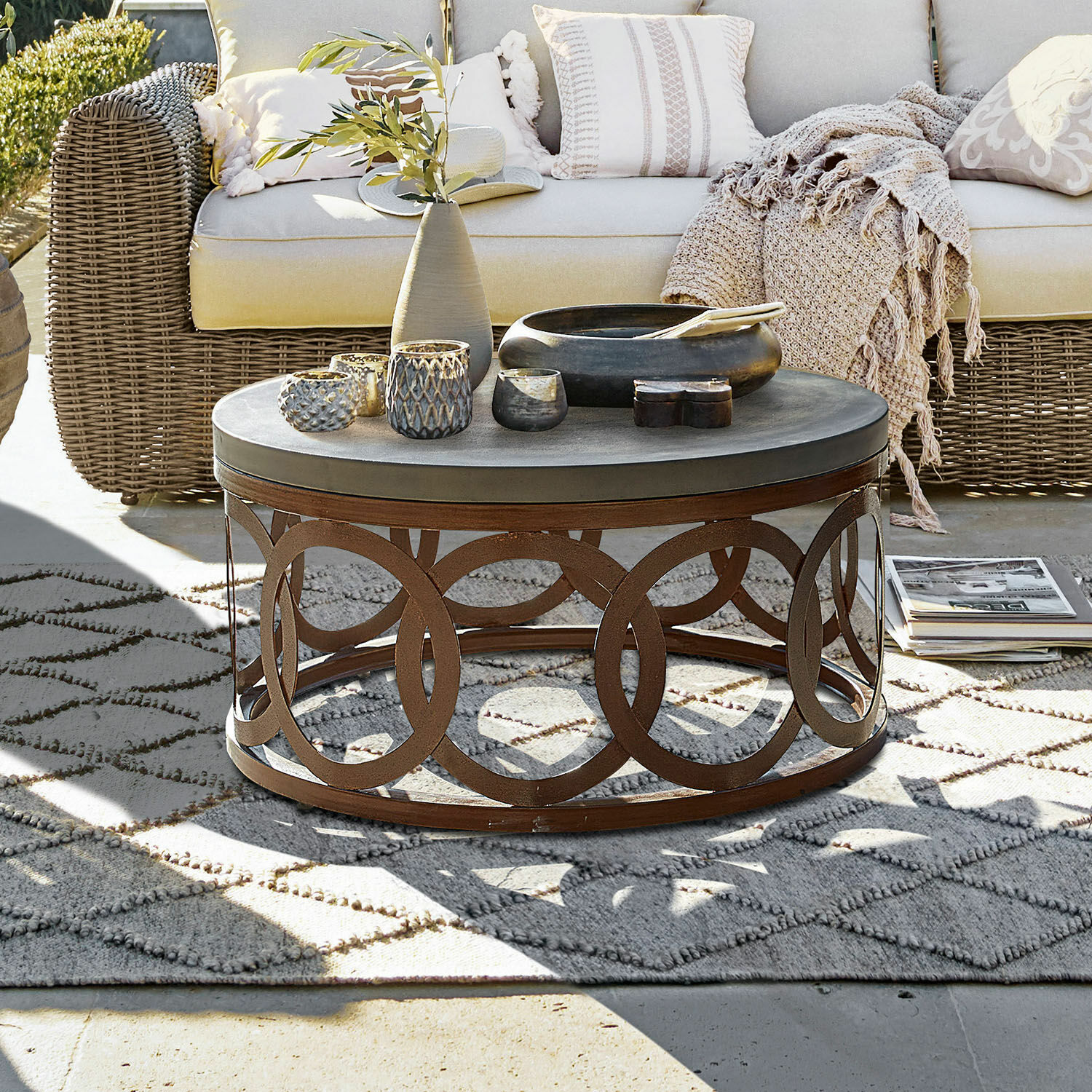 Couchtisch Boécourt Runder Couchtisch mit rostfarbener Metallbasis und grauer Tischplatte auf der Terrasse mit Korbsofa