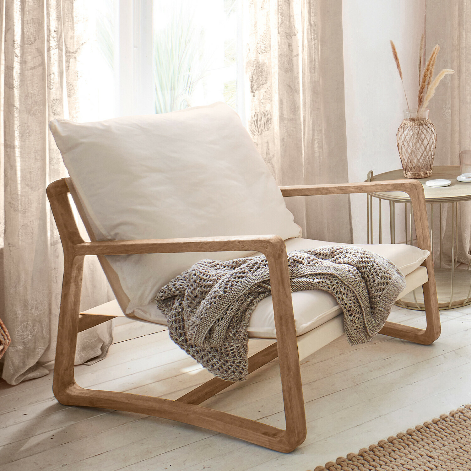 Sessel aus hellem Holz mit cremefarbenem Kissen und grauer Strickdecke in hellem Wohnzimmer