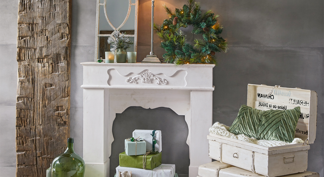 Weisser dekorativer Kamin mit grünem Tannenzweigkranz und grünen Kissen, festliche Weihnachtsdekoration