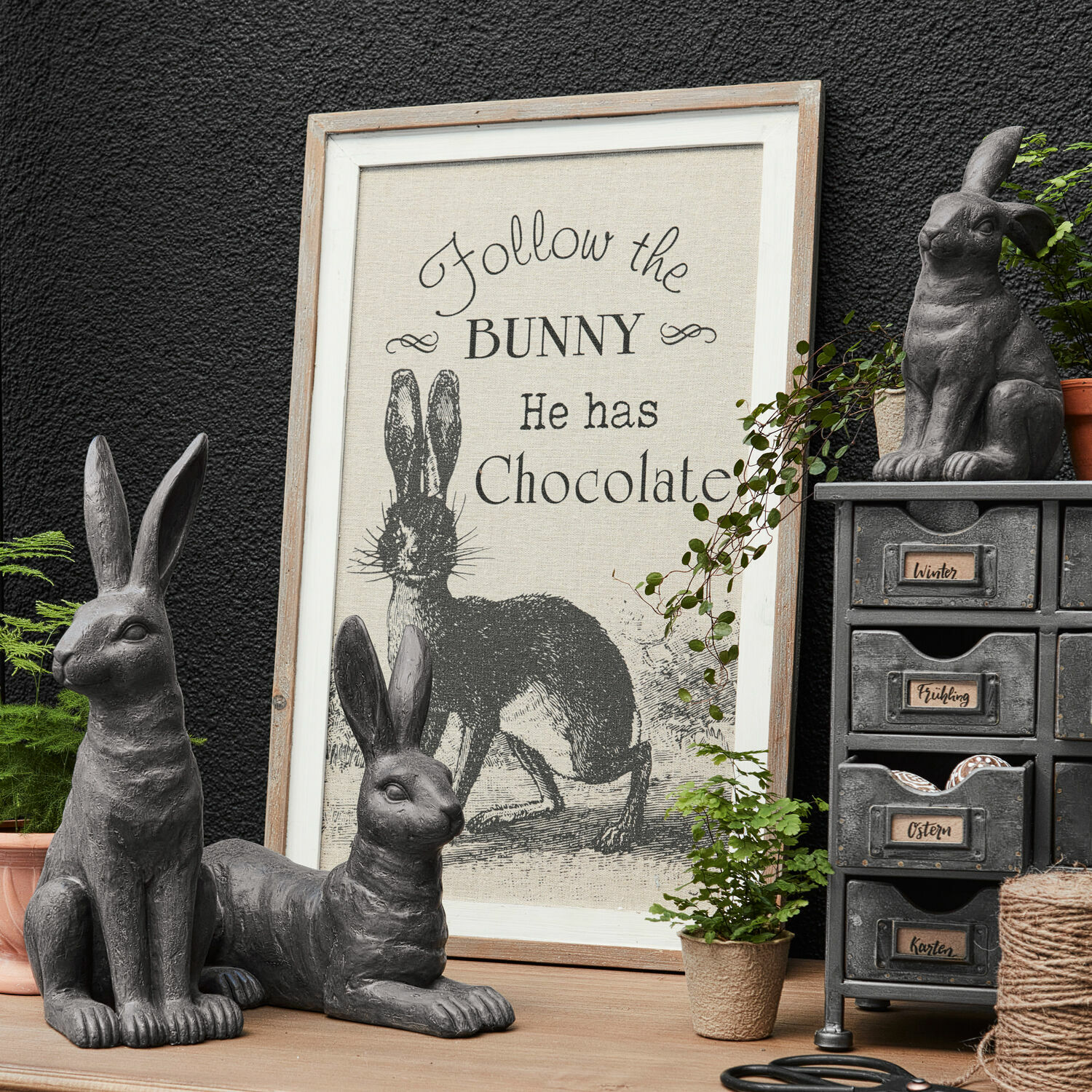 Dekoboard Chocolate Graue Hasenfiguren als Dekoration mit Rahmen und Schriftzug über Hasen und Schokolade auf Holztisch