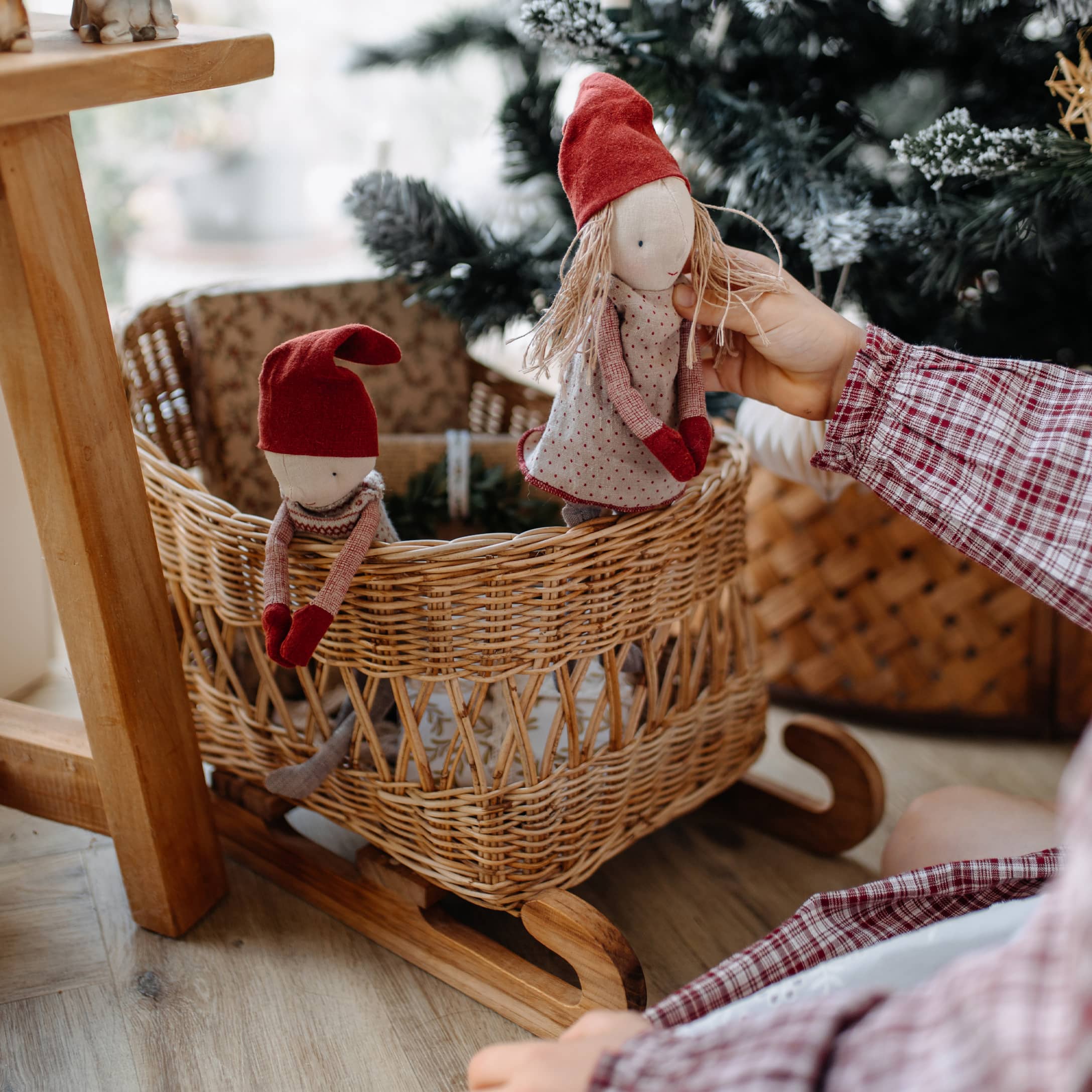 Holzschaukel mit Weidenkorb und zwei Puppen mit roten Mützen, weihnachtliche Dekoration