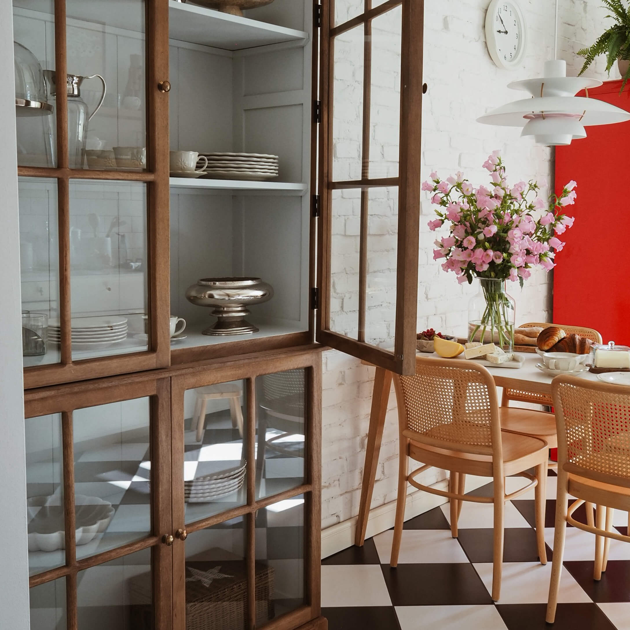 Helles Esszimmer mit Holzvitrine, rosa Blumen und schwarz-weiß kariertem Boden