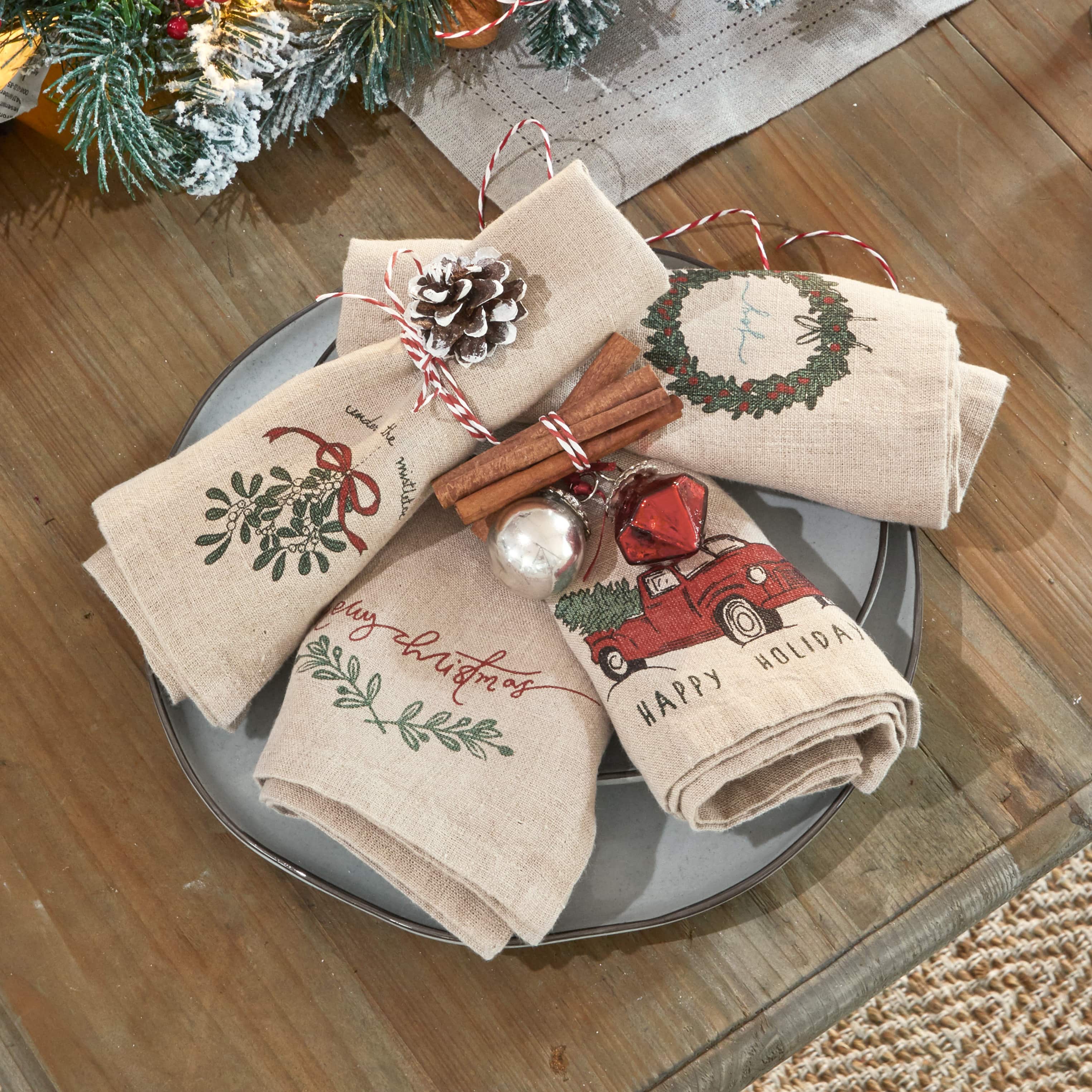 Leinen-Servietten mit Weihnachtsmotiven, verziert mit Zimtstangen und Tannenzapfen auf grauem Teller