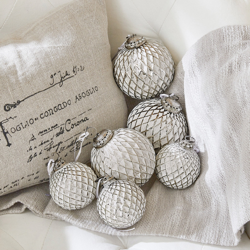Sechs silberne Christbaumkugeln aus Glas auf beiger Decke und Kissen arrangiert