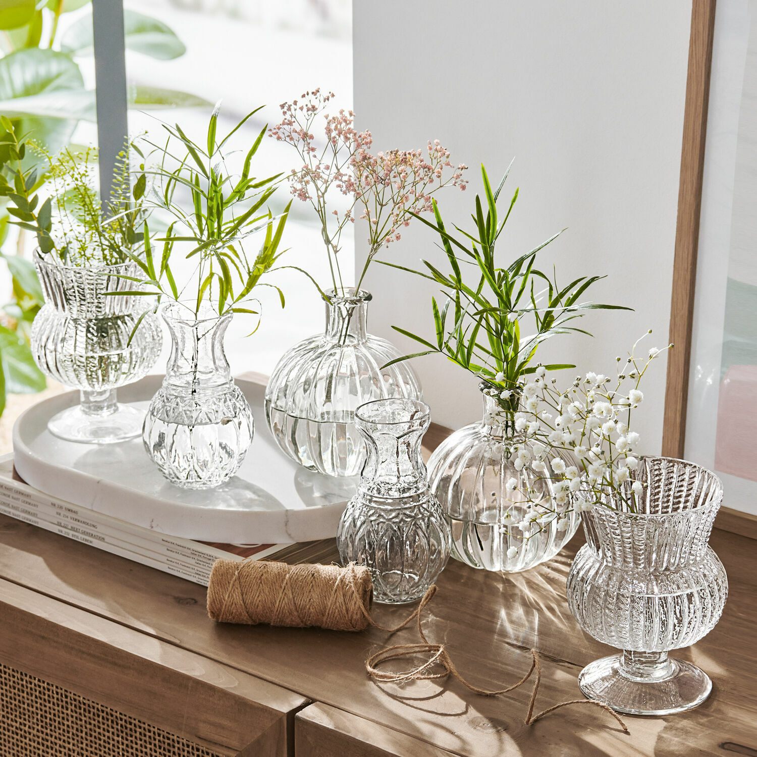 Vase 6er Set Amber Set aus transparenten Glasvasen mit grünen und weissen Blumen auf Holzkommode