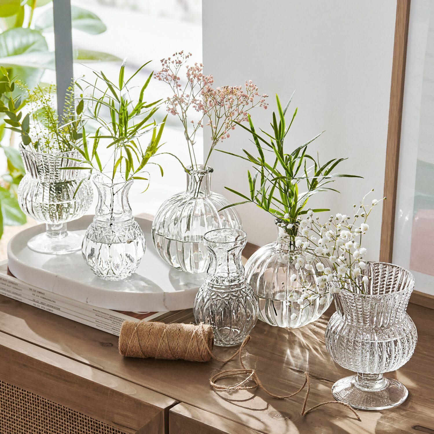 Vase 6er Set Amber Set aus transparenten Glasvasen mit grünen und weissen Blumen auf Holzkommode