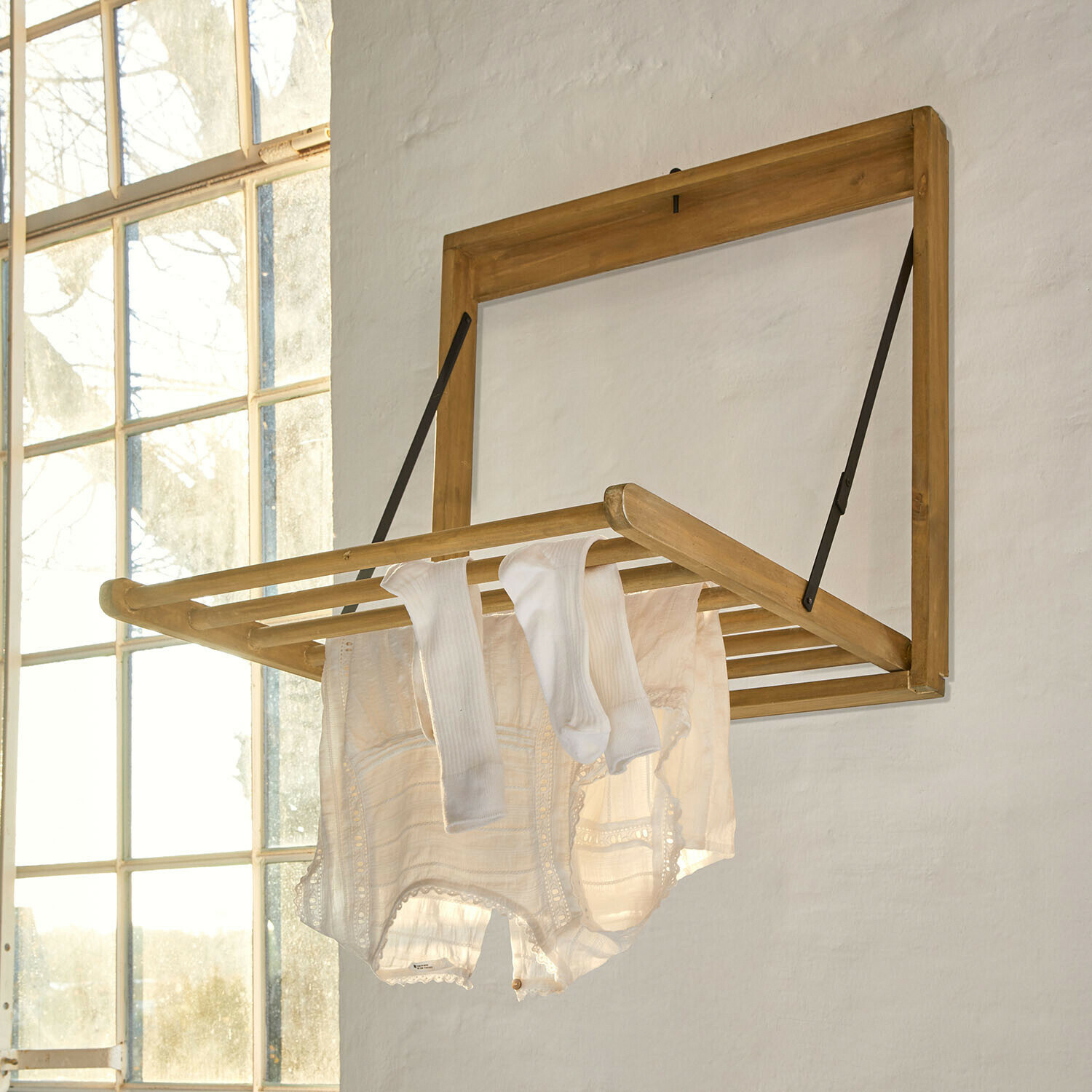 Wandklappbarer Wäscheständer aus hellem Holz mit weissen Kleidungsstücken in hellem Raum