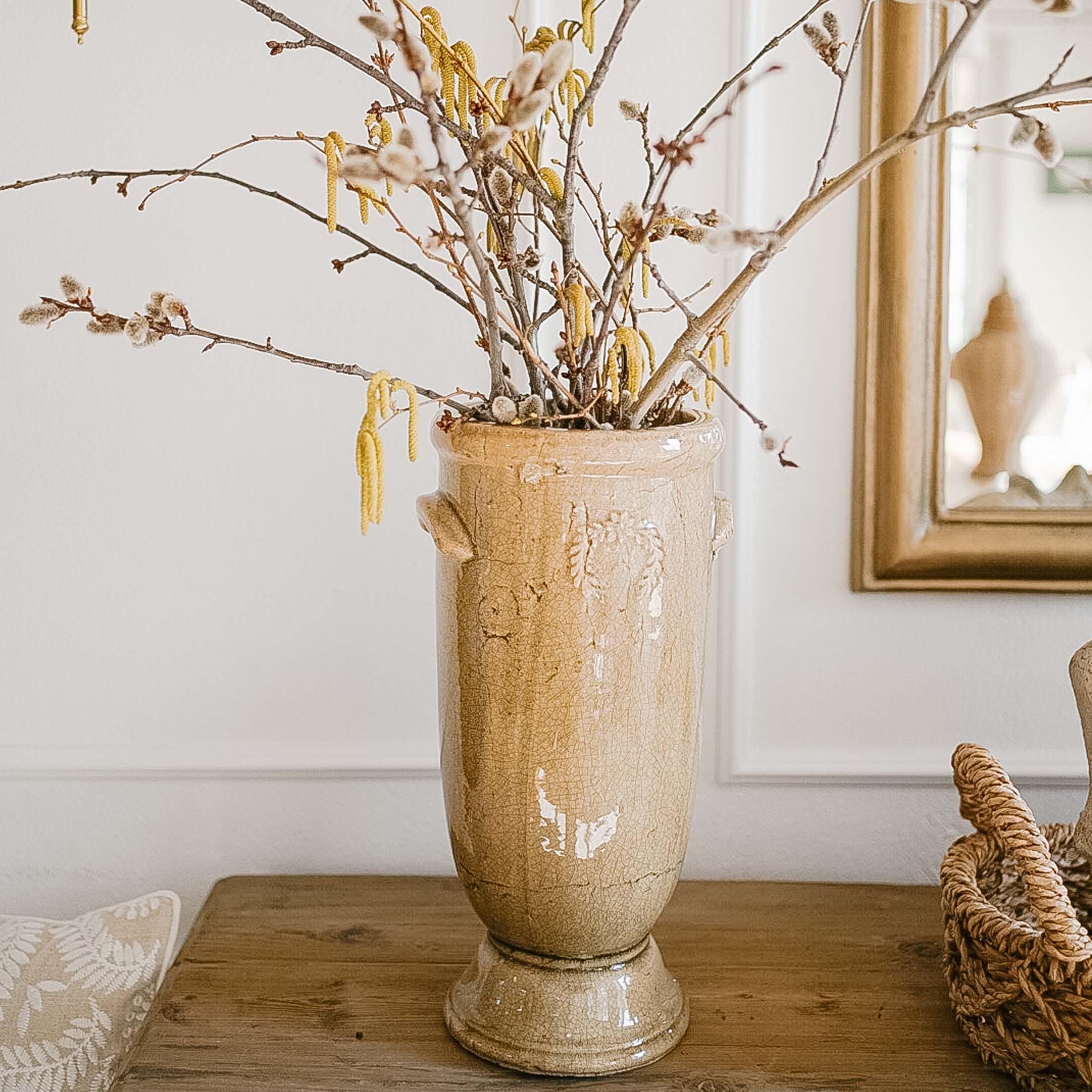 Beige Keramikvase mit Blumen und Zweigen auf Holztisch in hellem Raum