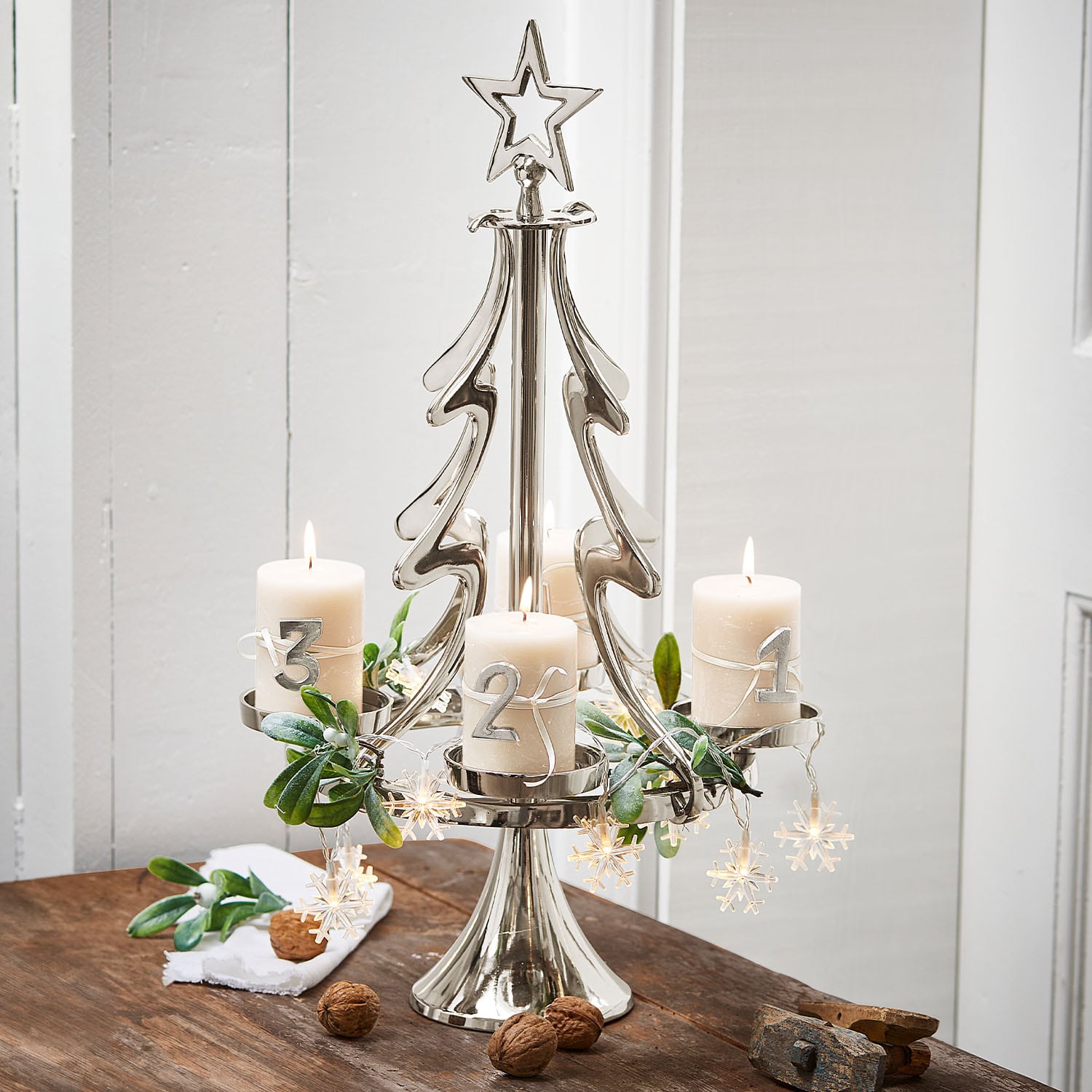 Metall-Adventskranz in Tannenbaumform mit vier weissen Kerzen und Weihnachtsdeko auf Holztisch