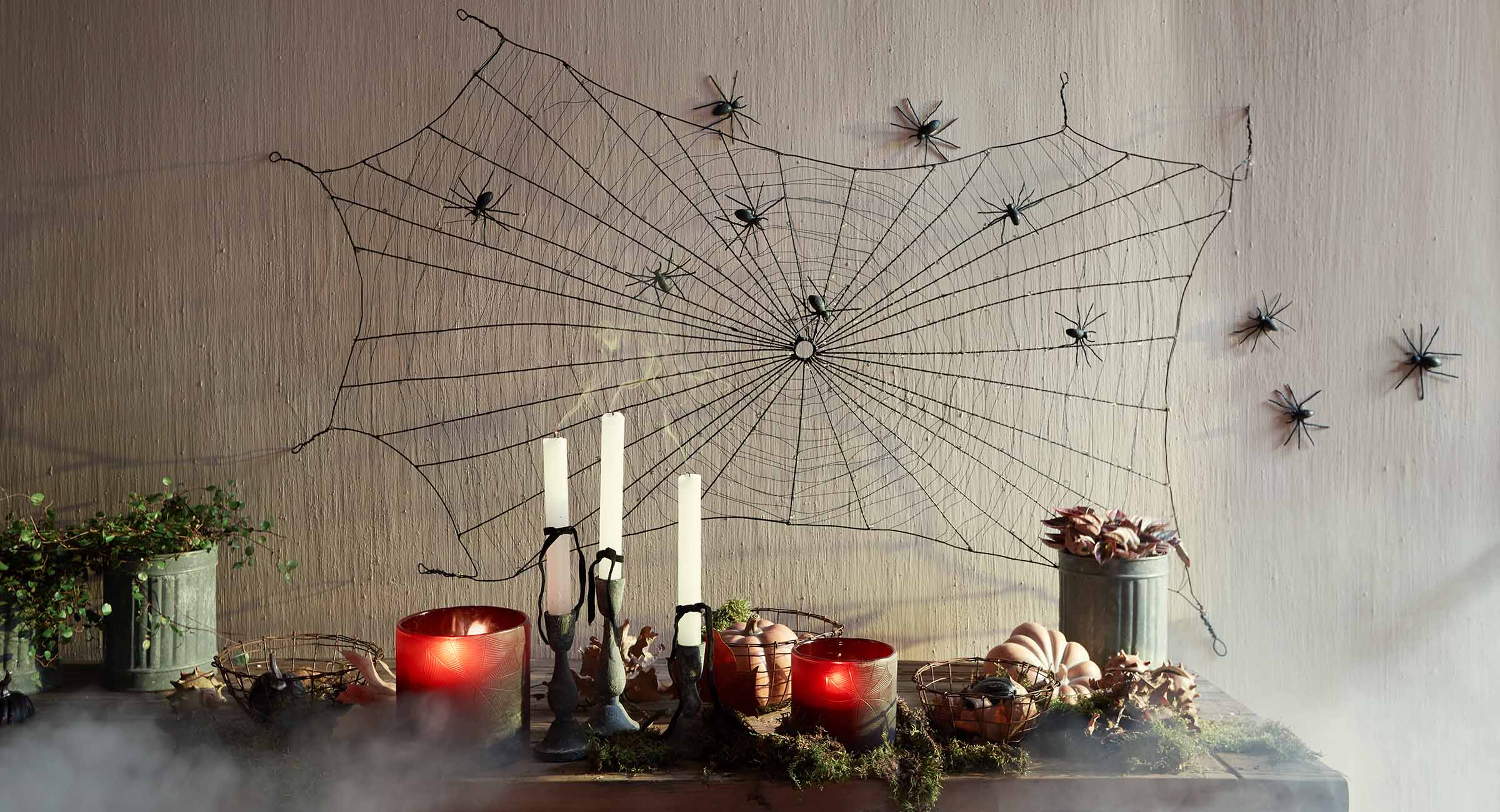 Halloween-Dekoration mit schwarzem Spinnennetz und Spinnen an der Wand, Kerzen und Kürbissen auf dem Tisch