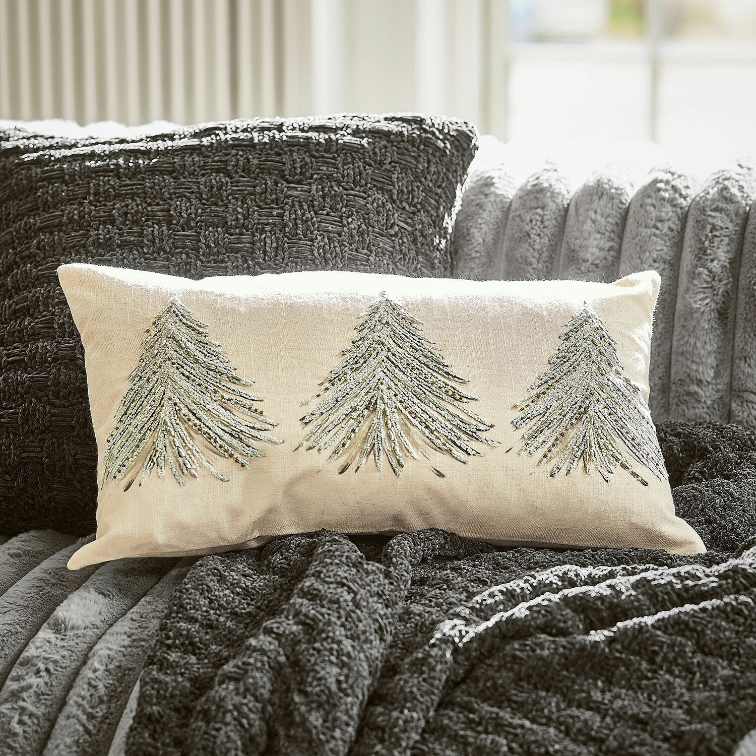 Kissenhülle Amandique Beige Dekokissen mit silbernen Tannenbaum-Stickereien auf dunkelgrauer Decke und Sofa