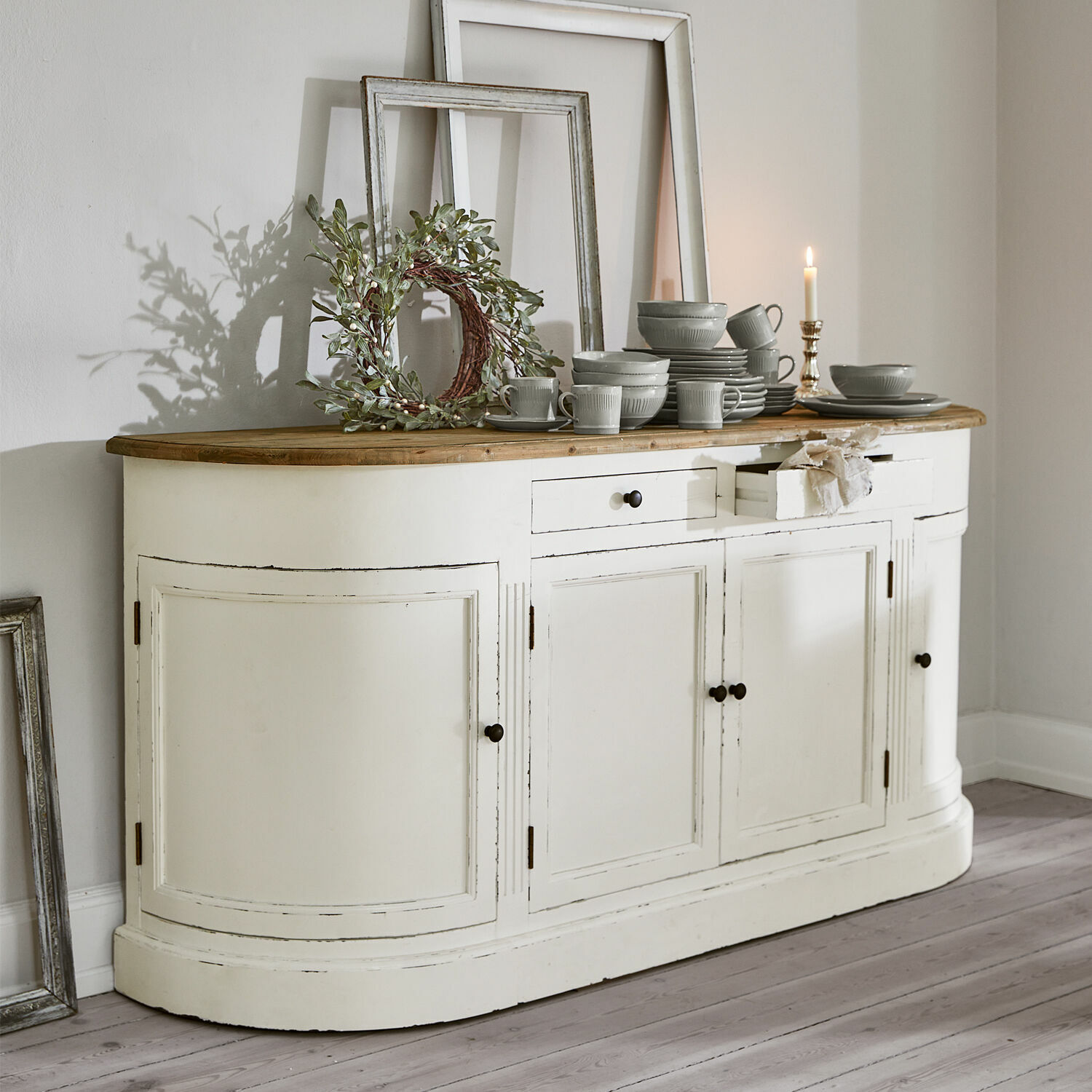 Sideboard Louisiana Weisse Holzkommode mit Holzplatte und grauem Geschirr darauf, Wanddekorationen im Hintergrund