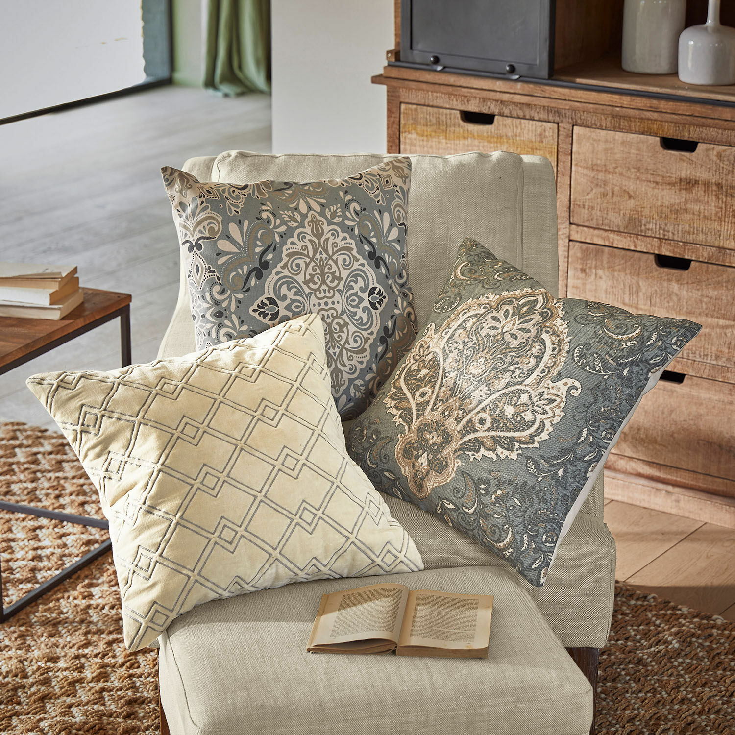 Drei dekorative Kissen mit beigen und grauen Mustern auf einem hellen Sessel im Wohnzimmer