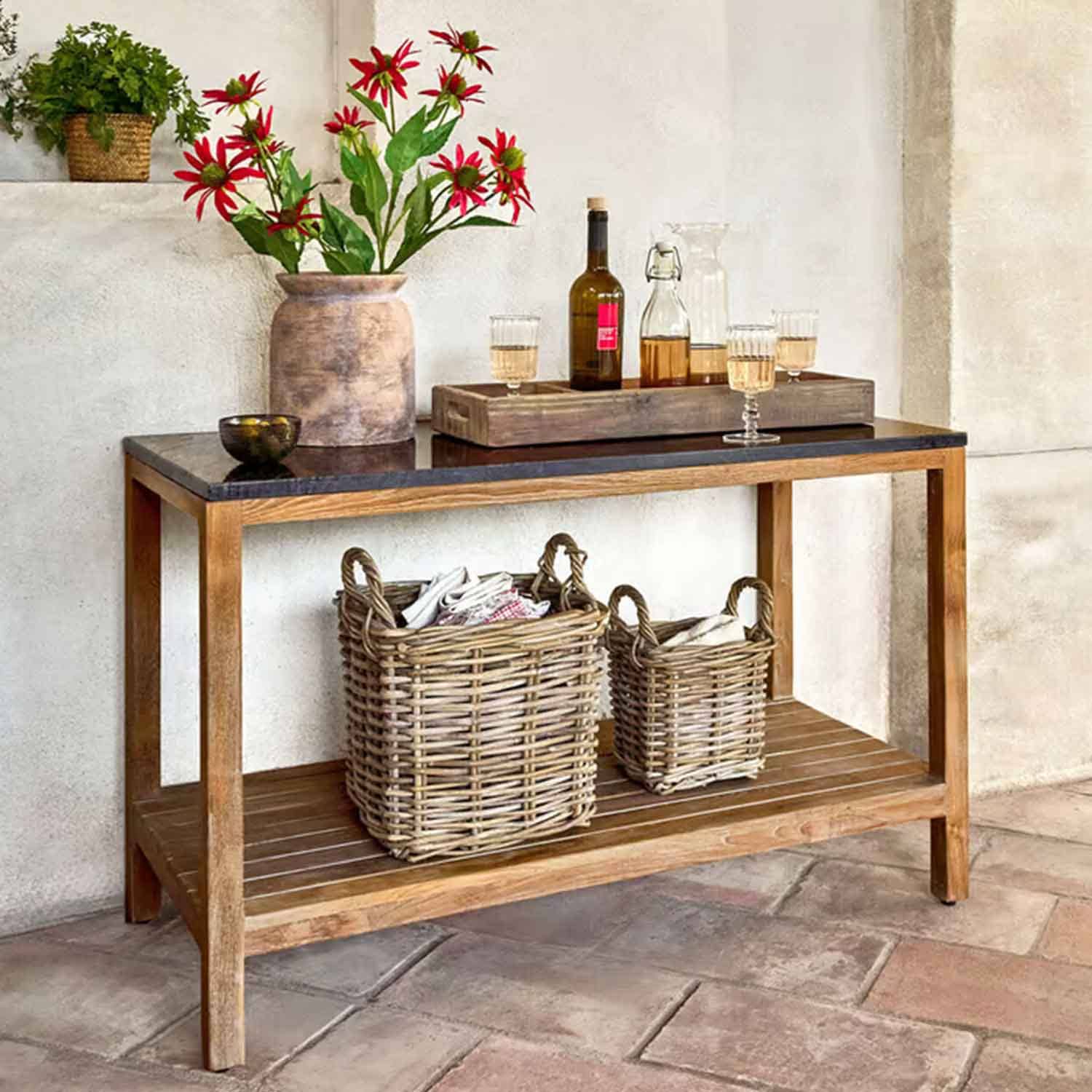 Holztisch mit schwarzer Platte, Vase mit roten Blumen und zwei geflochtenen Körben darunter in rustikalem Raum