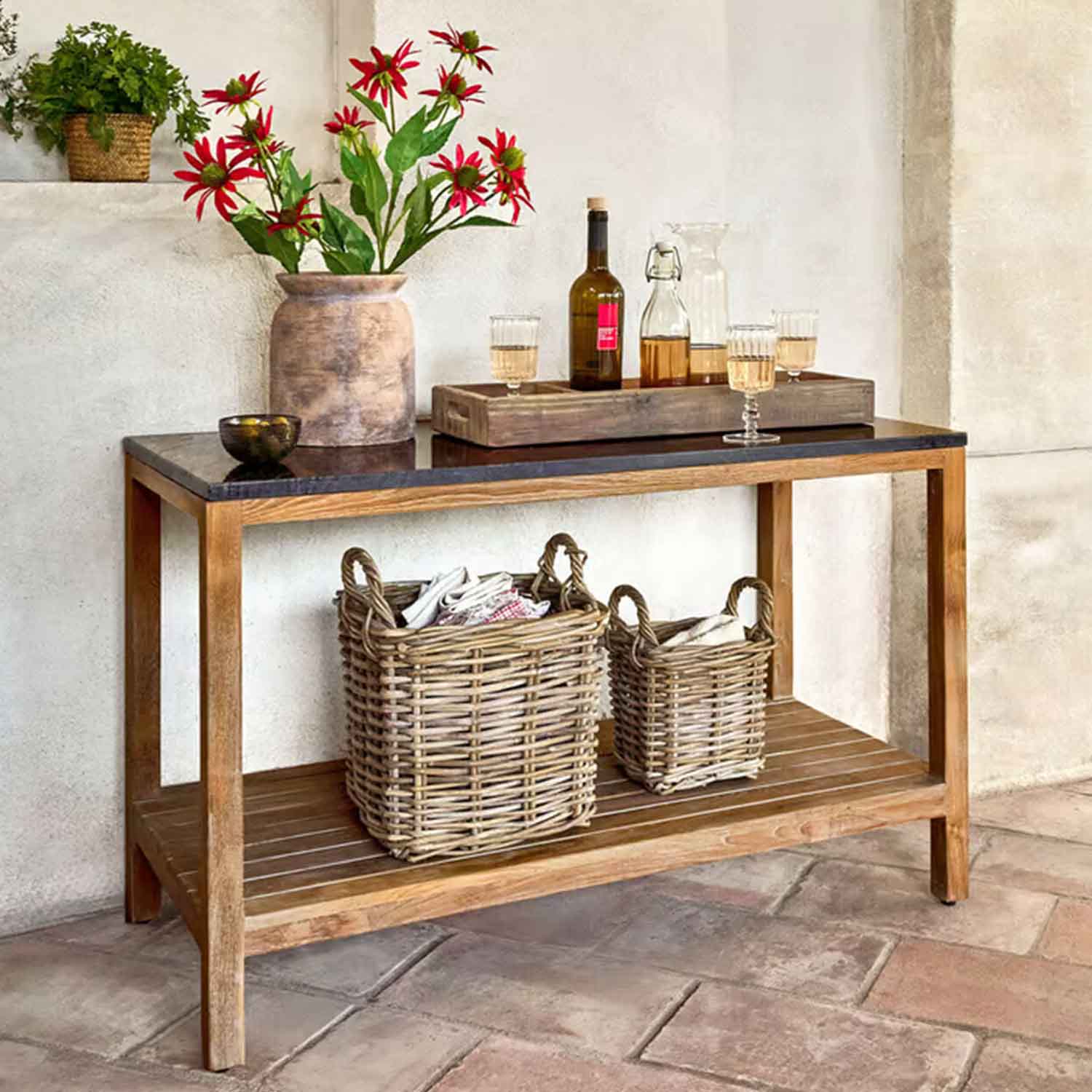 Holztisch mit schwarzer Platte, Vase mit roten Blumen und zwei geflochtenen Körben darunter in rustikalem Raum
