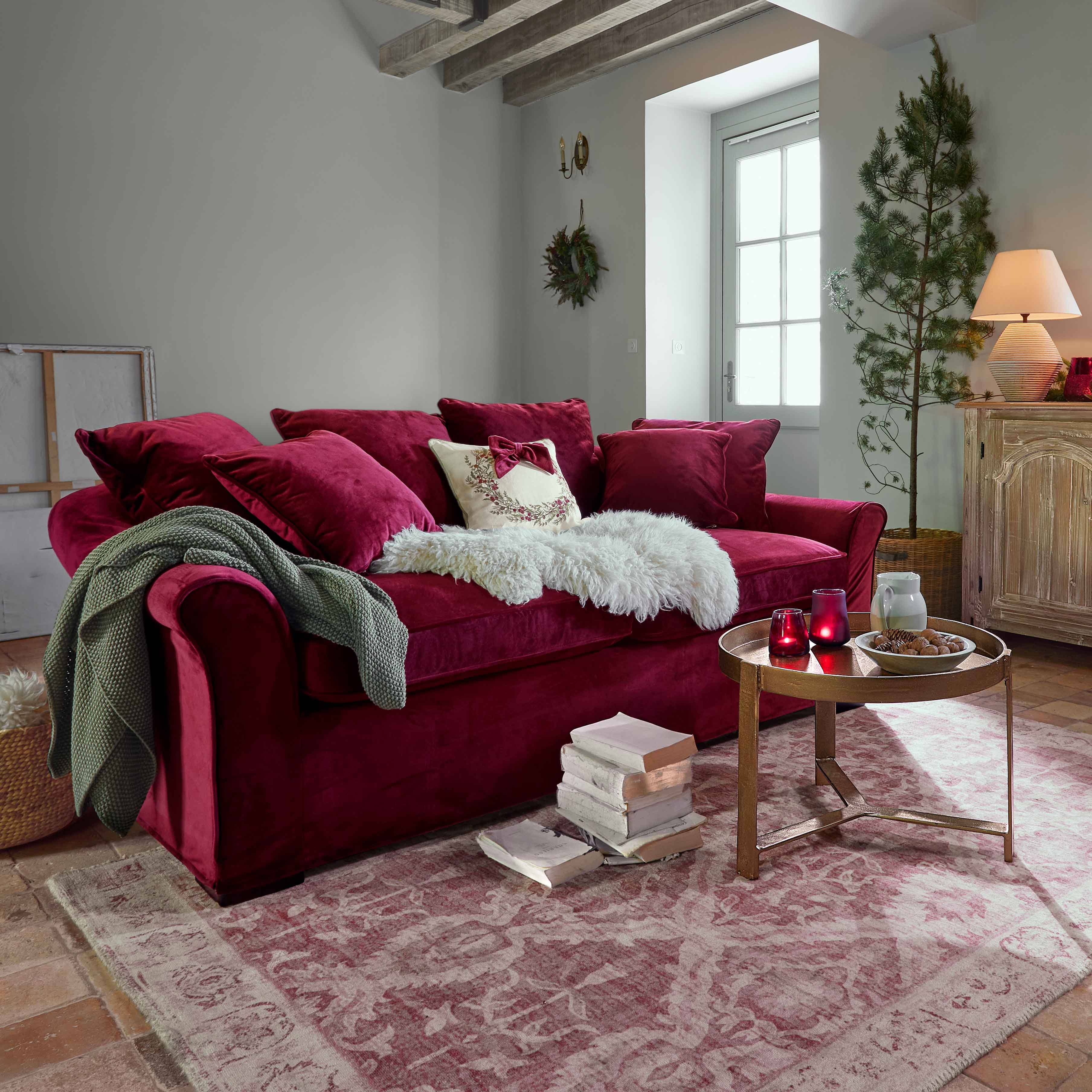 Bordeauxrotes Samtsofa mit Kissen und weicher Decke in gemütlichem Wohnzimmer mit Holzbalken