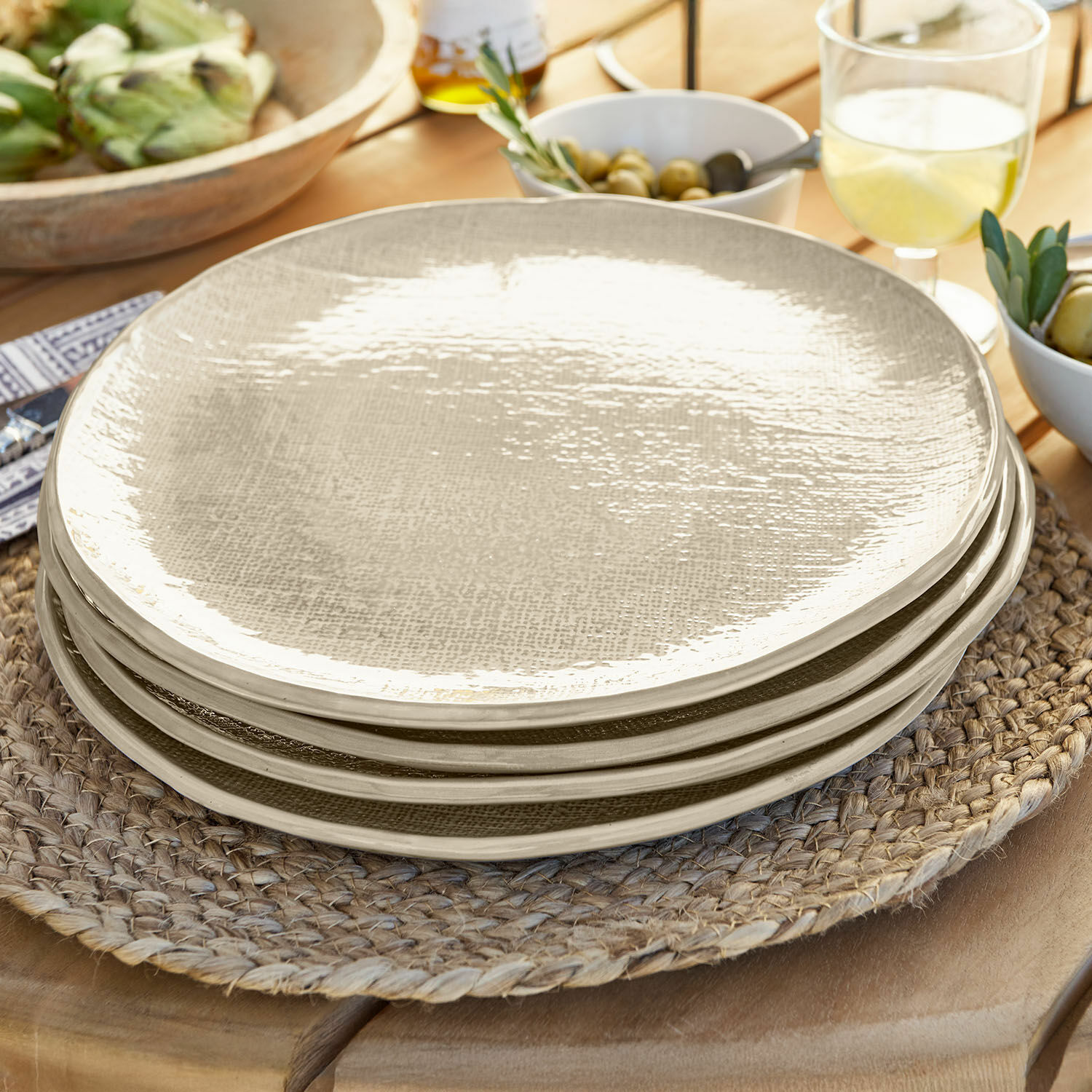 Set aus beigen, strukturierten Keramiktellern auf geflochtenem Platzset aus Holz