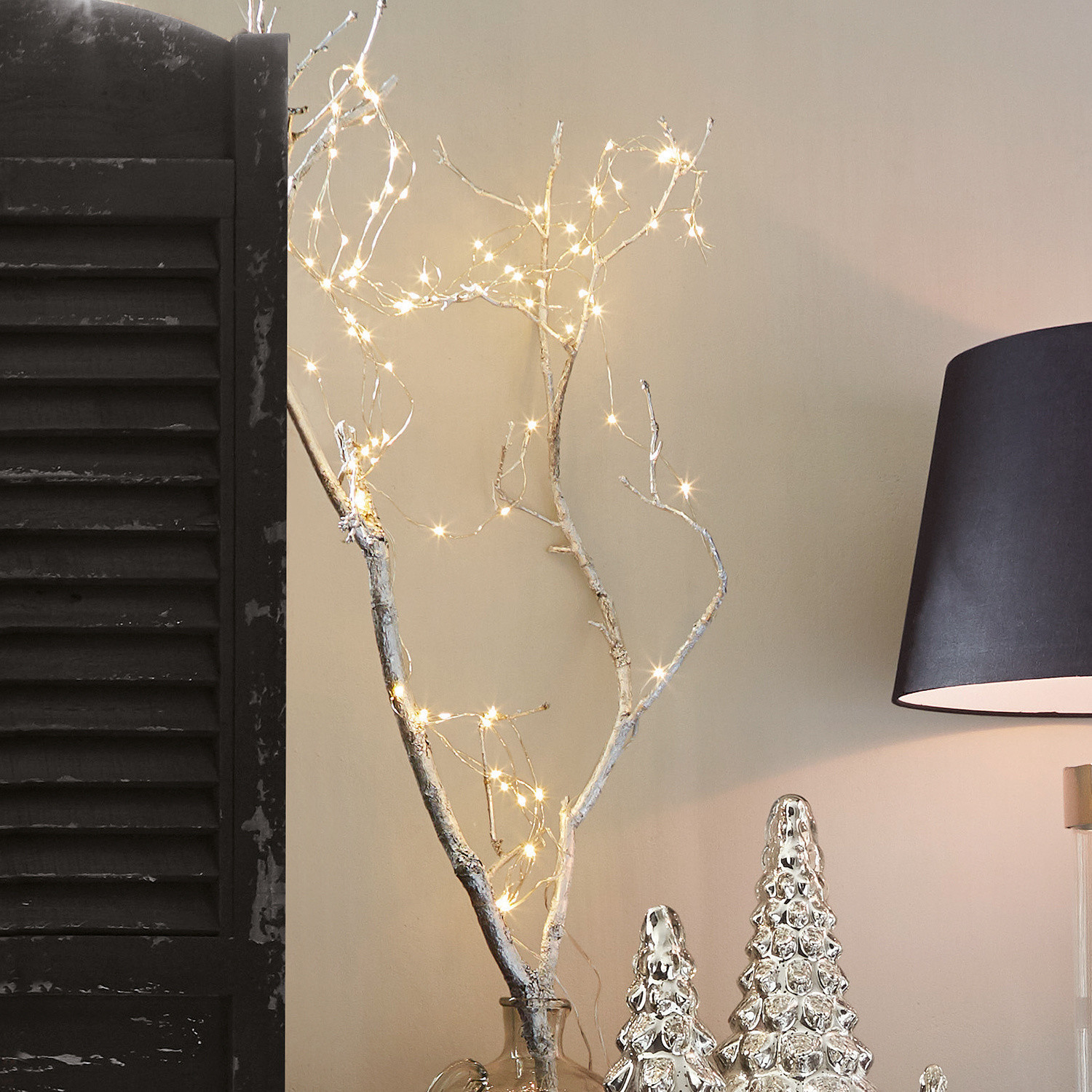 Lichterkette Loperhet Dekorativer Ast mit LED-Lichterkette in einer klaren Glasvase neben silberner Weihnachtsdekoration und schwarzer Lampe
