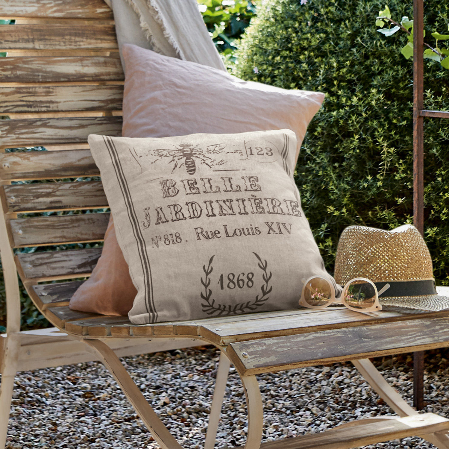Kissenhülle Abelle Beiges Leinenkissen mit Vintage-Druck auf verwitterter Holzbank im Garten mit Sonnenhut und Brille