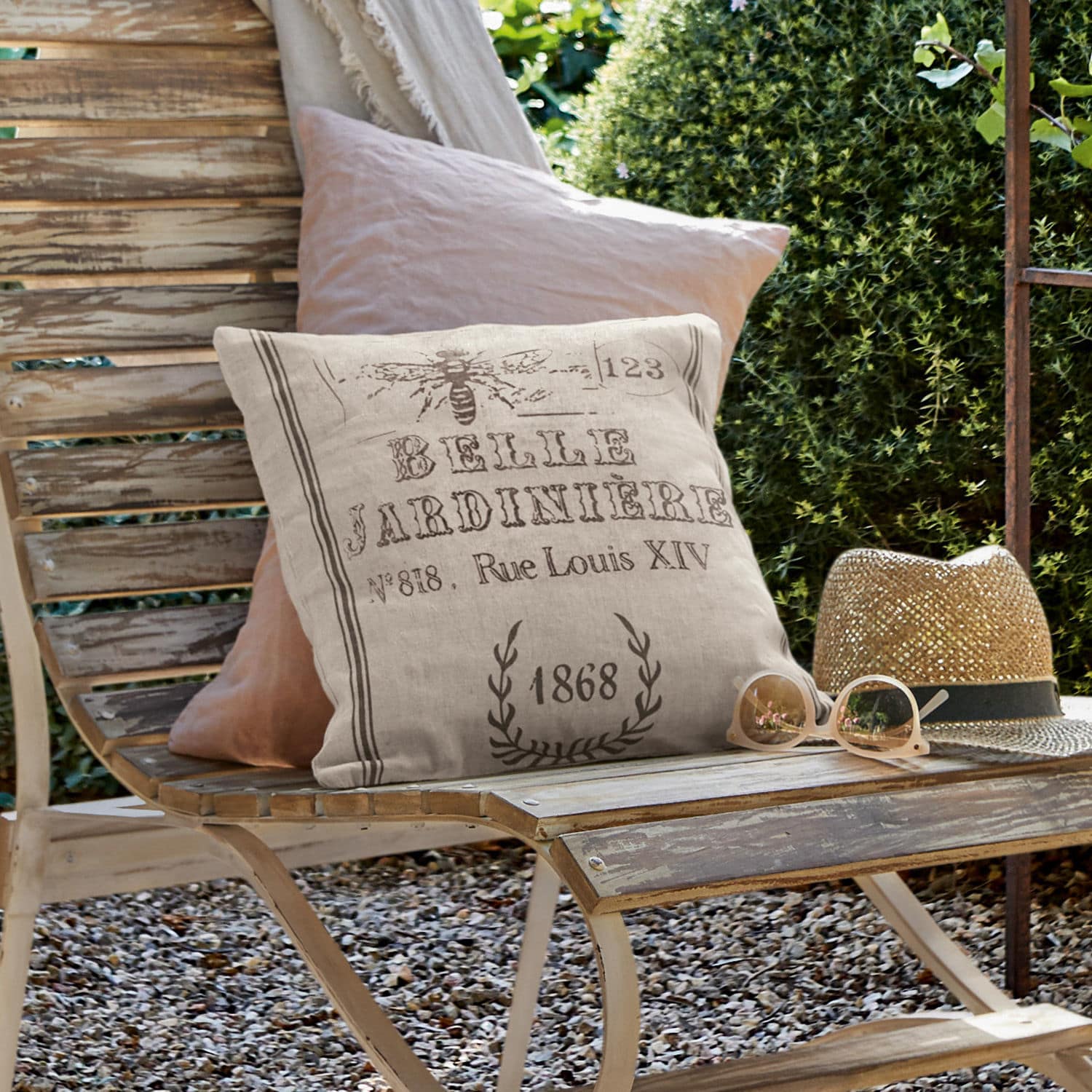 Kissenhülle Abelle Beiges Leinenkissen mit Vintage-Druck auf verwitterter Holzbank im Garten mit Sonnenhut und Brille