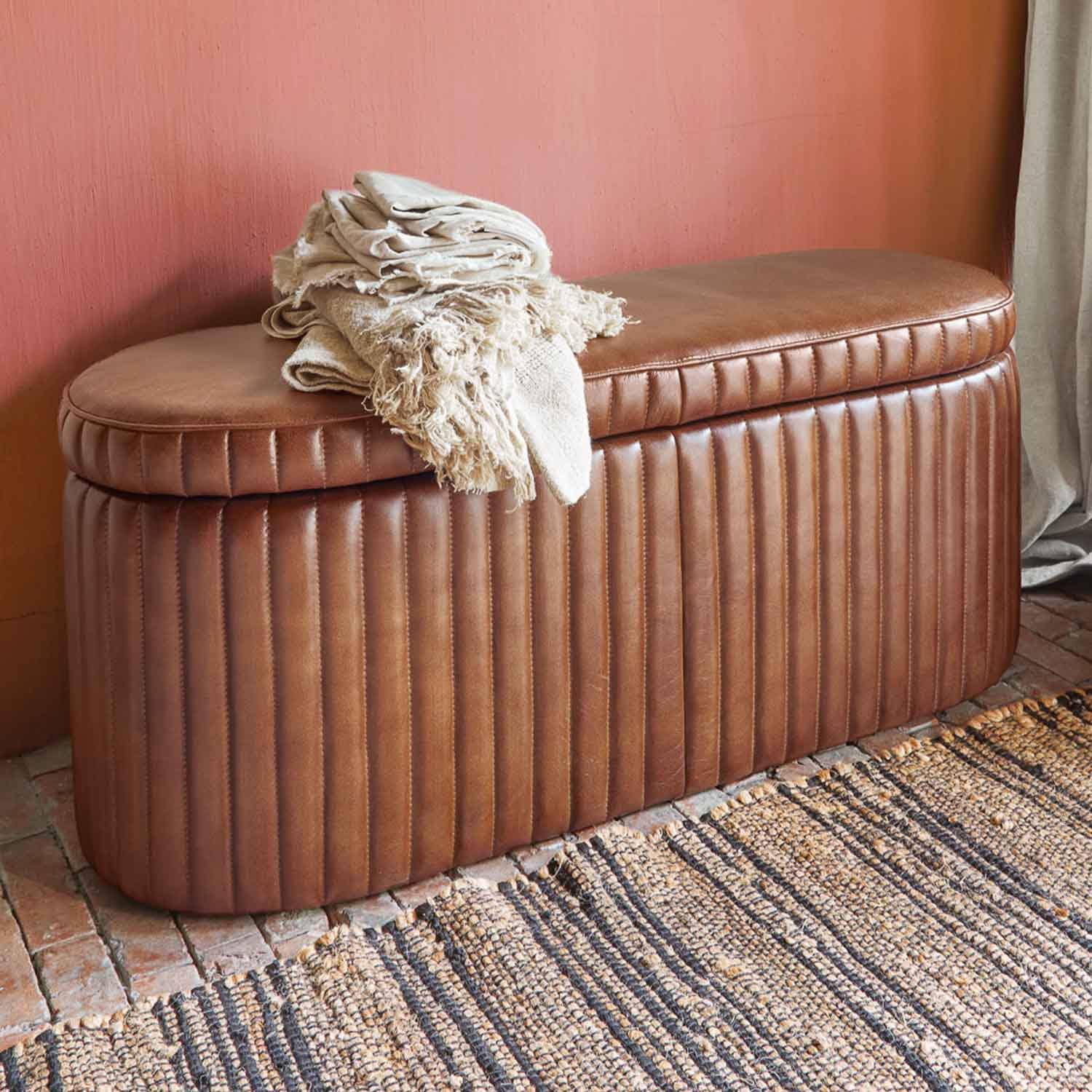 Braune, gesteppte Leder-Bank mit cremefarbenen Decken vor rosa Wand und Teppich