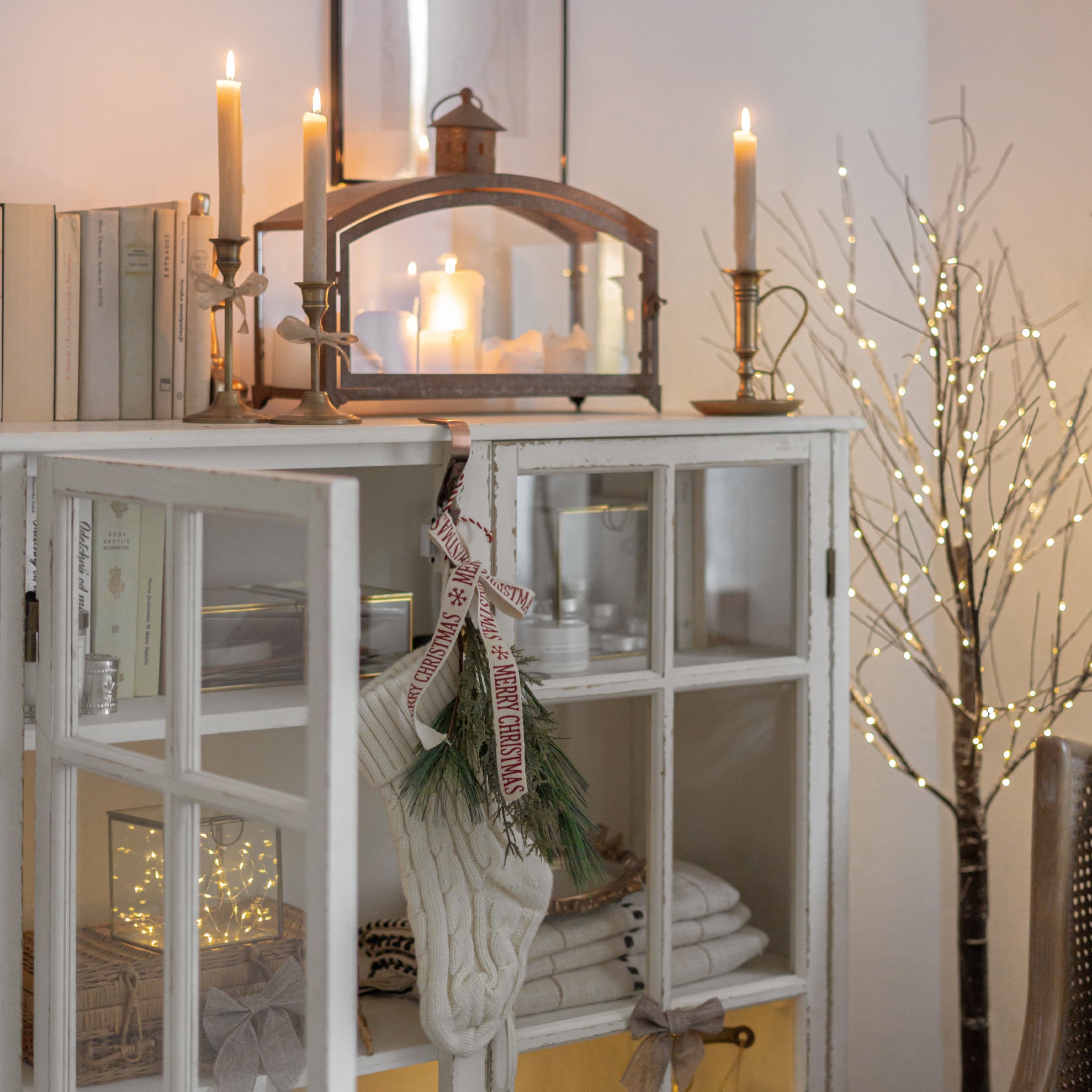Weisse gestrickte Weihnachtssocke mit grünen Zweigen an weissem Schrank mit Kerzen und Lichterzweig